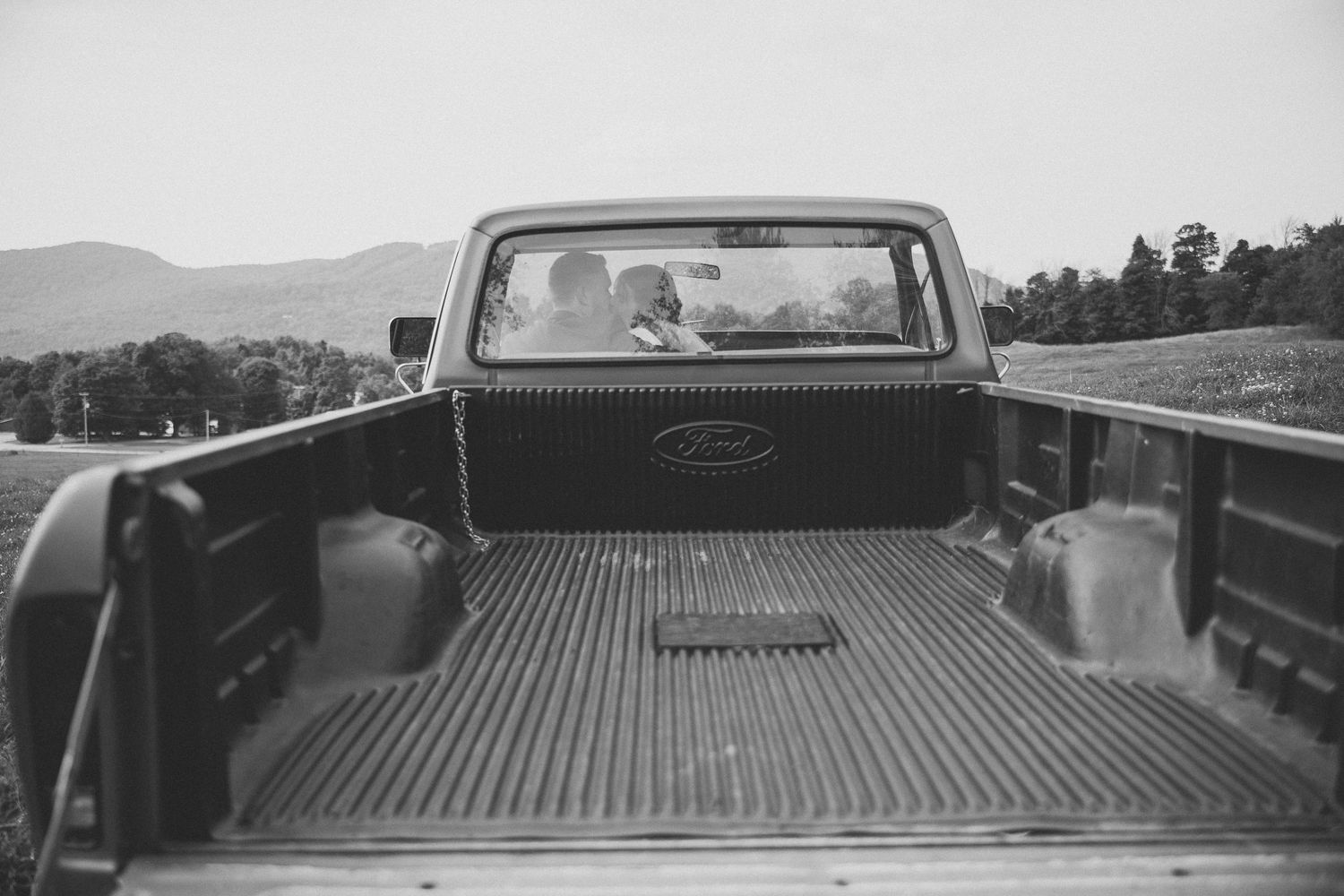 Photo en noir et blanc de la benne d’un pickup, montrant le plancher métallique nervuré et le hayon avec maries qui s'embrassent