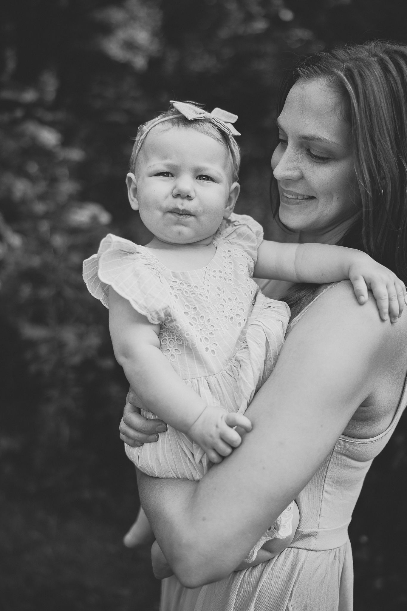 Portrait noir et blanc : parent tenant son enfant en robe claire avec nœud, capturé pour moments tendres et complicité familiale