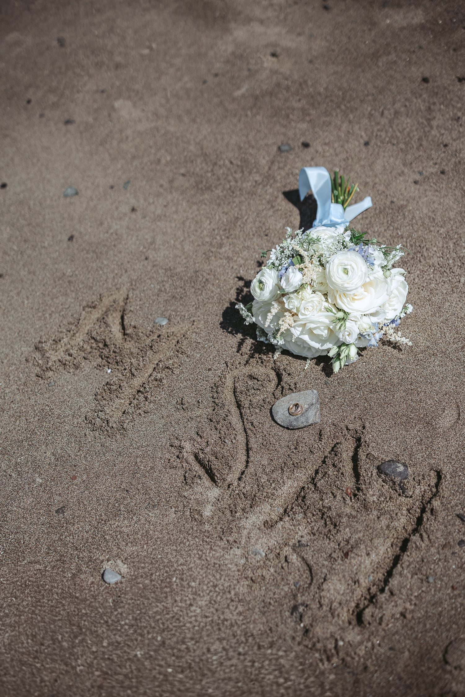 Bouquet déposé sur le sable avec les initiales des mariés
