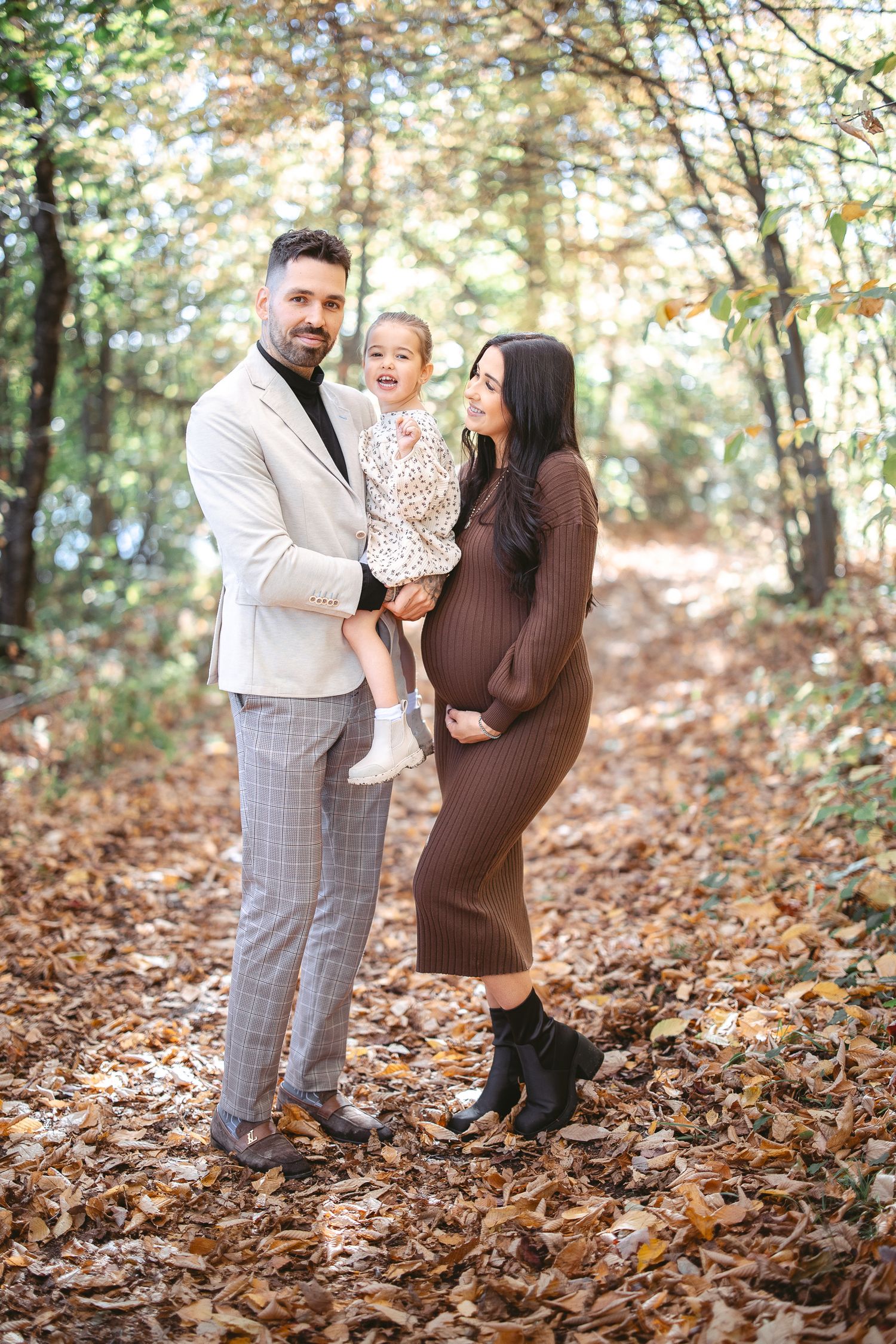A family stands together on a forest path covered in autumn leaves during a fall photoshoot.