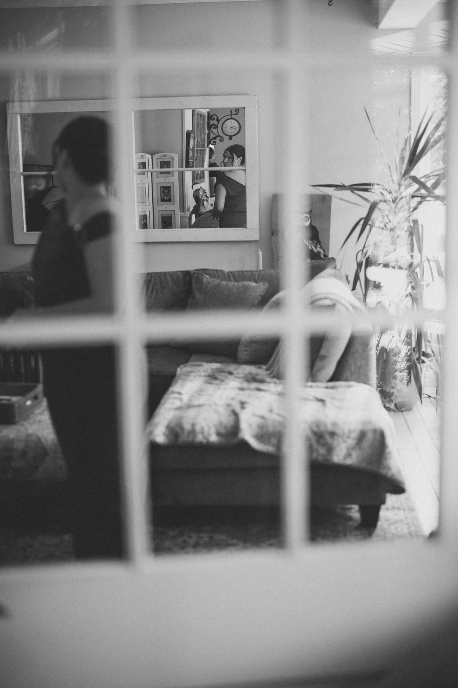 femme se regardant dans le mirroir, vue intérieure en noir et blanc à travers des vitres, canapé, œuvre encadrée et plante en pot