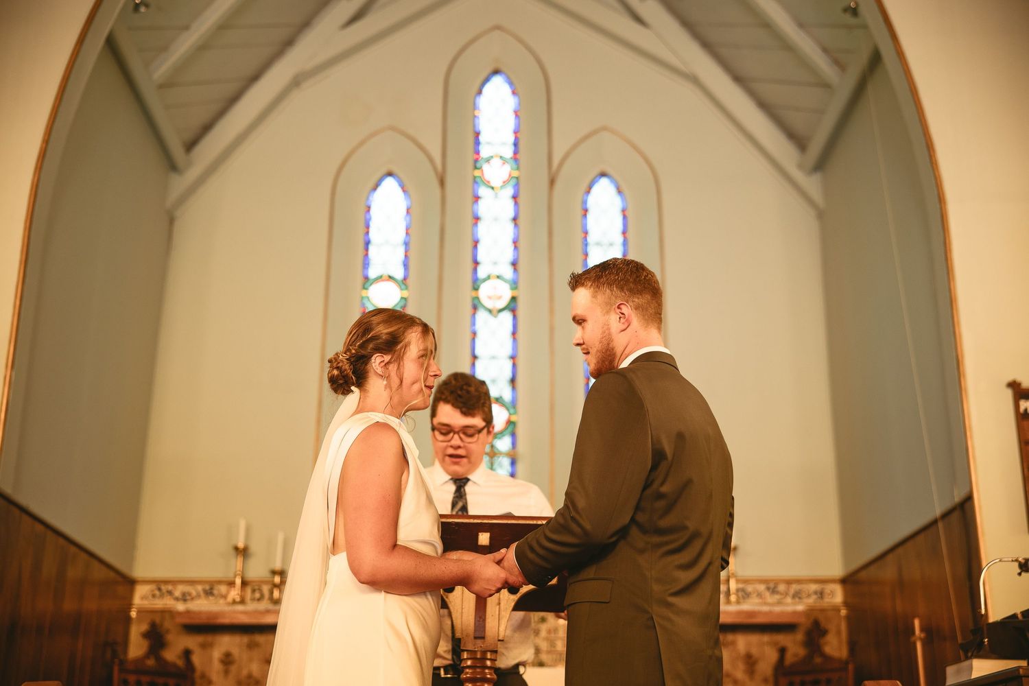 Couple qui échange leurs voeux lors de leur cérémonie de mariage dans une église aux vitraux, en Estrie