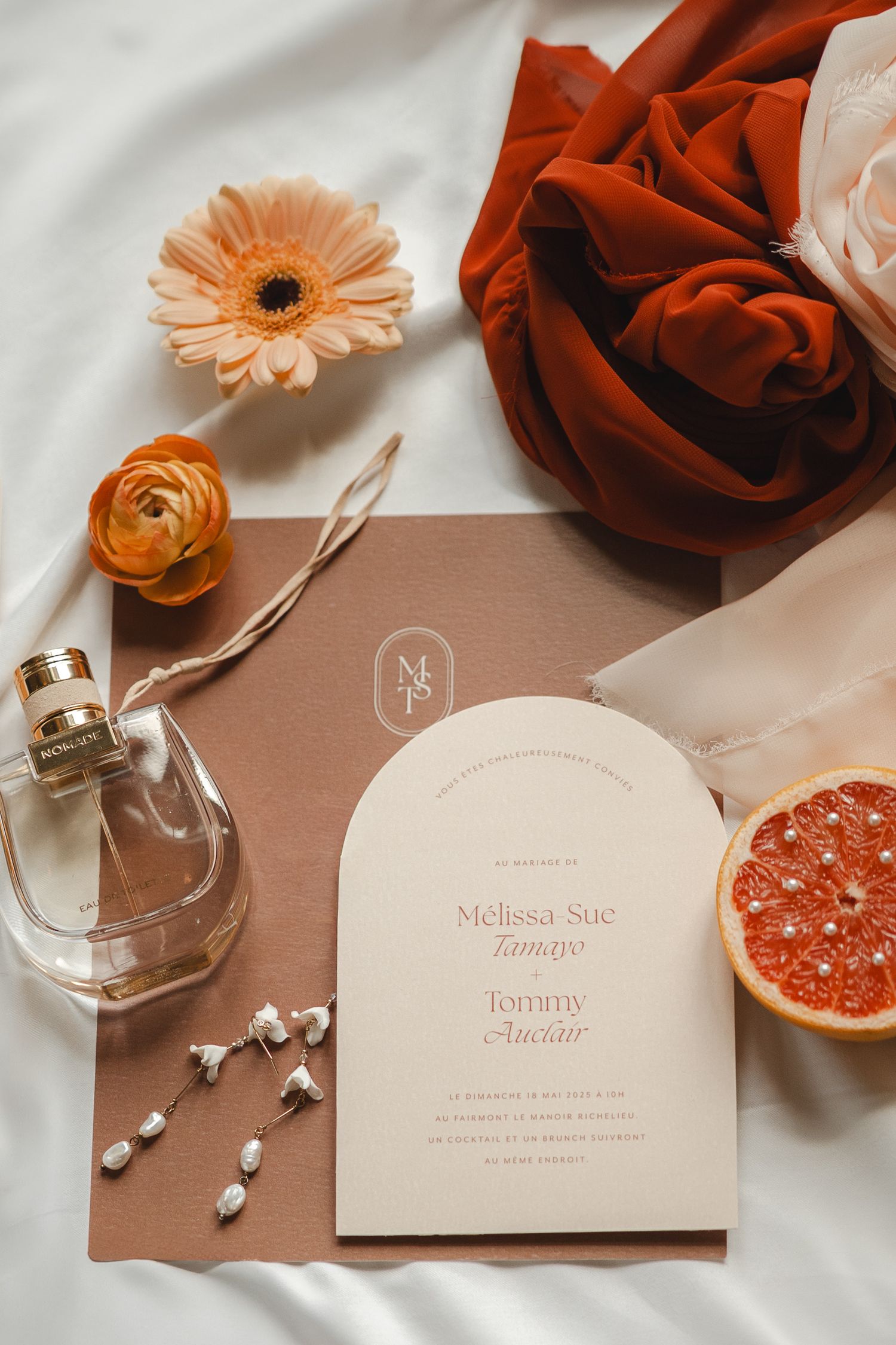 Wedding stationery layout with peach flowers, grapefruit slices, and elegant invitation cards on white and brown surfaces.
