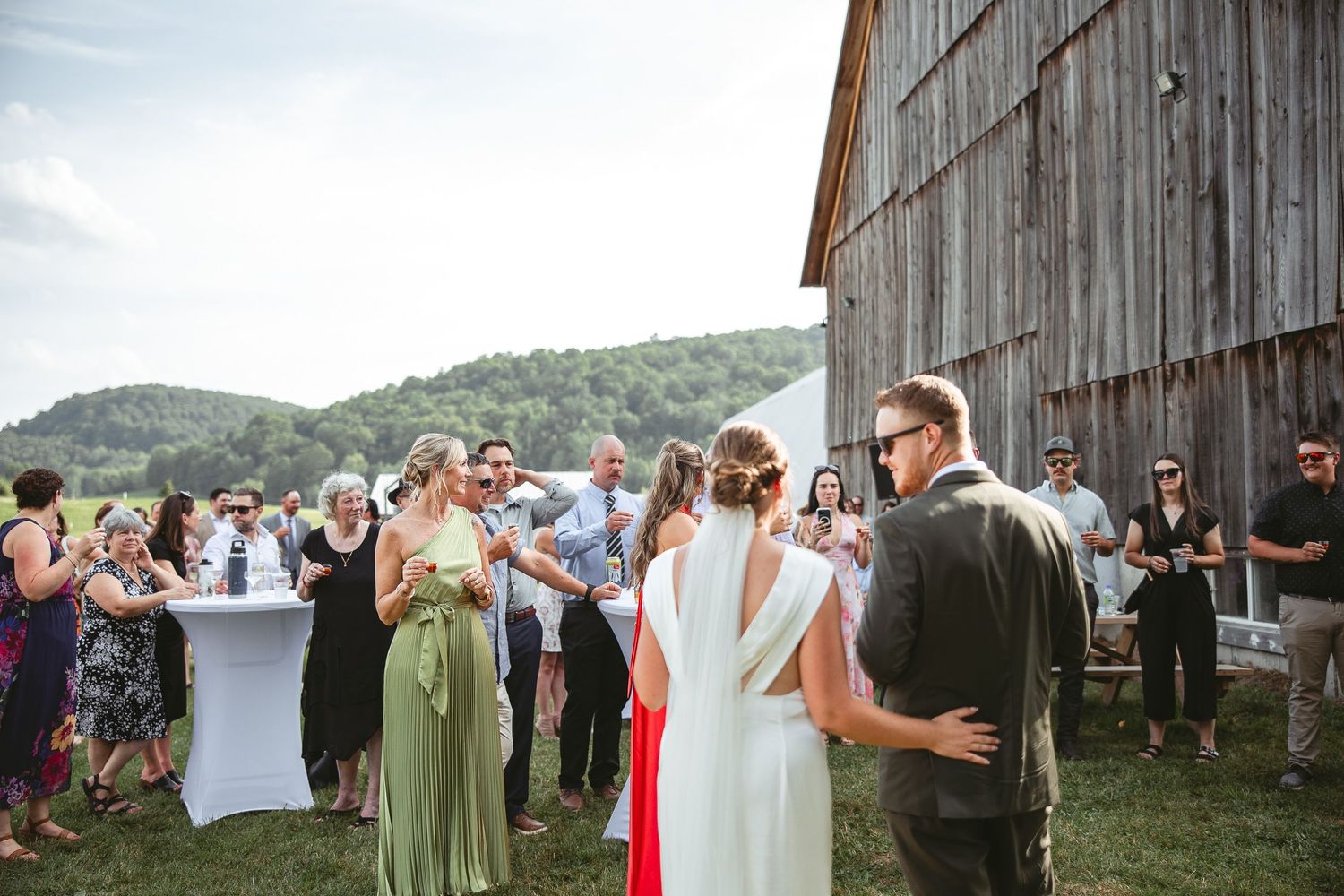 Invités de mariage rassemblés devant une grange en bois rustique, dans un décor montagneux pittoresque