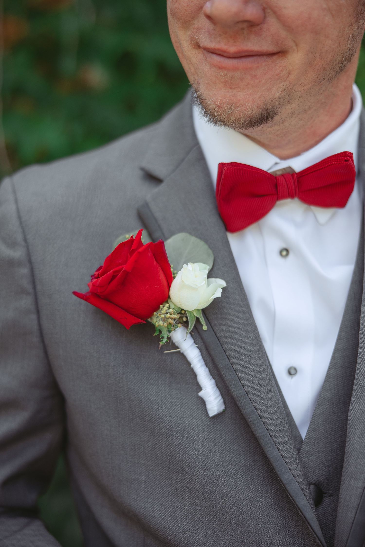 Groomsmen wearing gray suits and red bow ties with white and red rose boutonnieres in a wedding party.