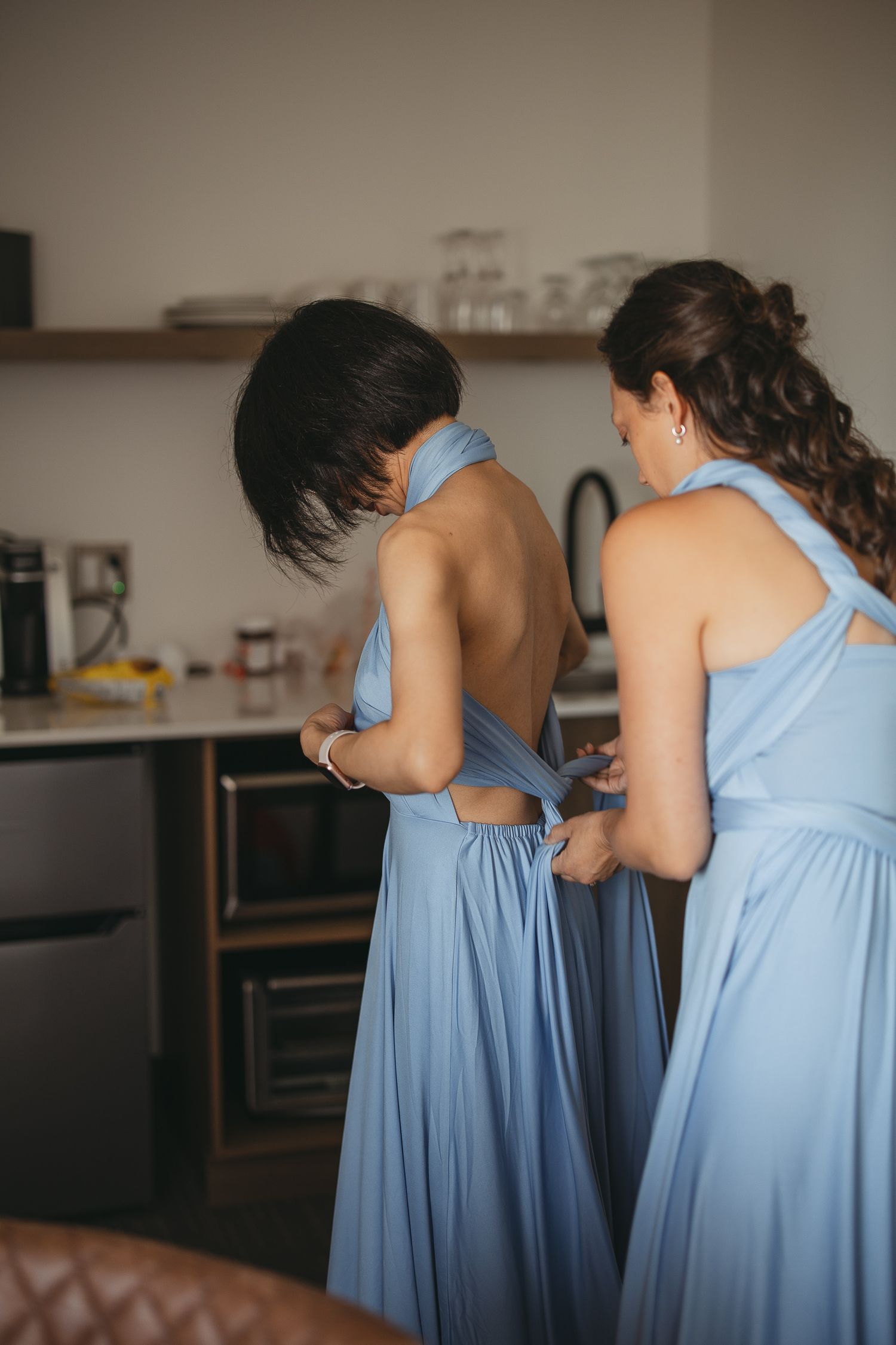Demoiselles d’honneur en robes bleu pâle lors des préparatifs du mariage, capturées dans un moment spontané et complice.