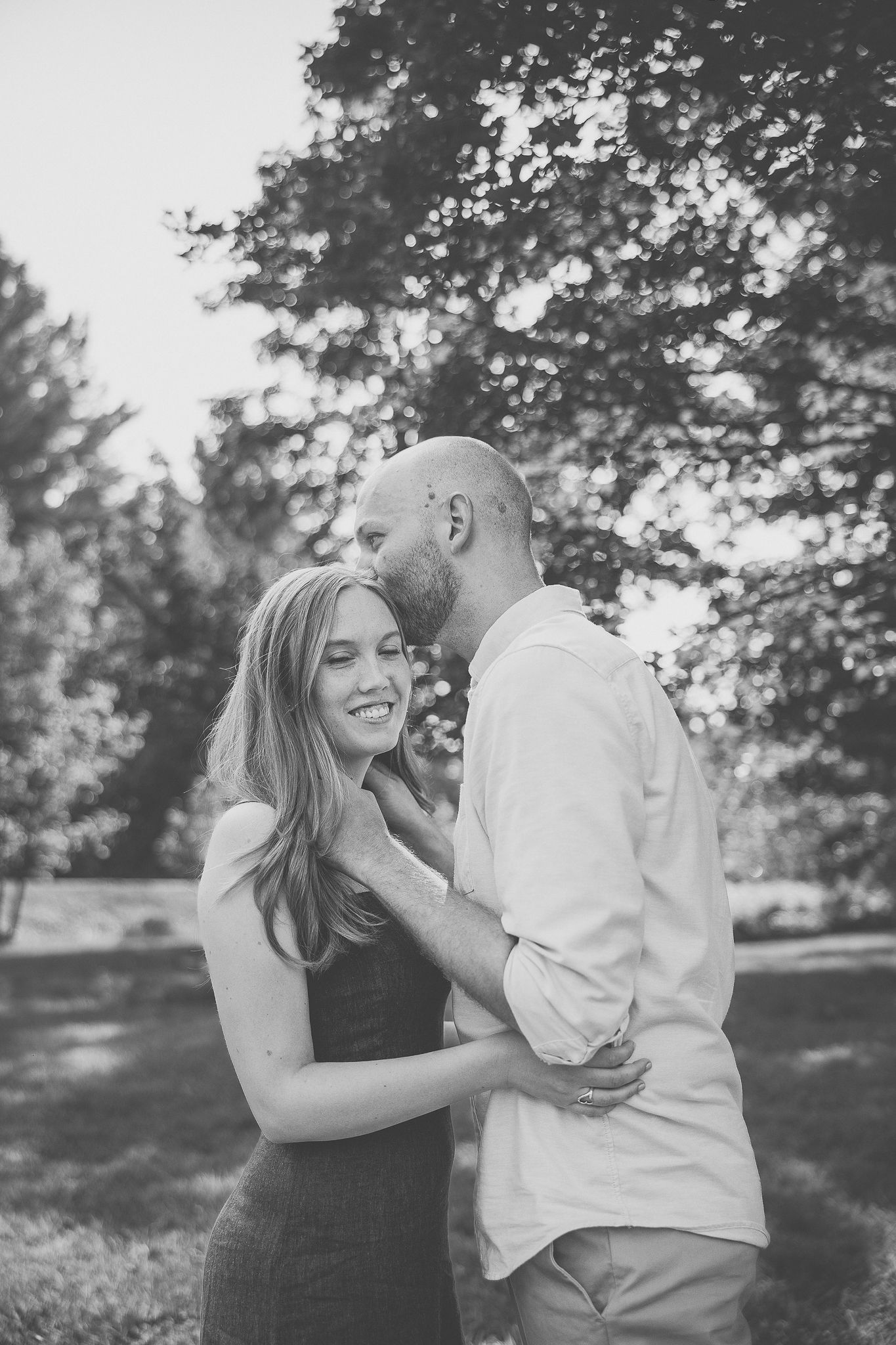 Photographie de couple en noir et blanc dans parc ensoleillé, riant et s’enlaçant, pour valoriser émotion et complicité romantique