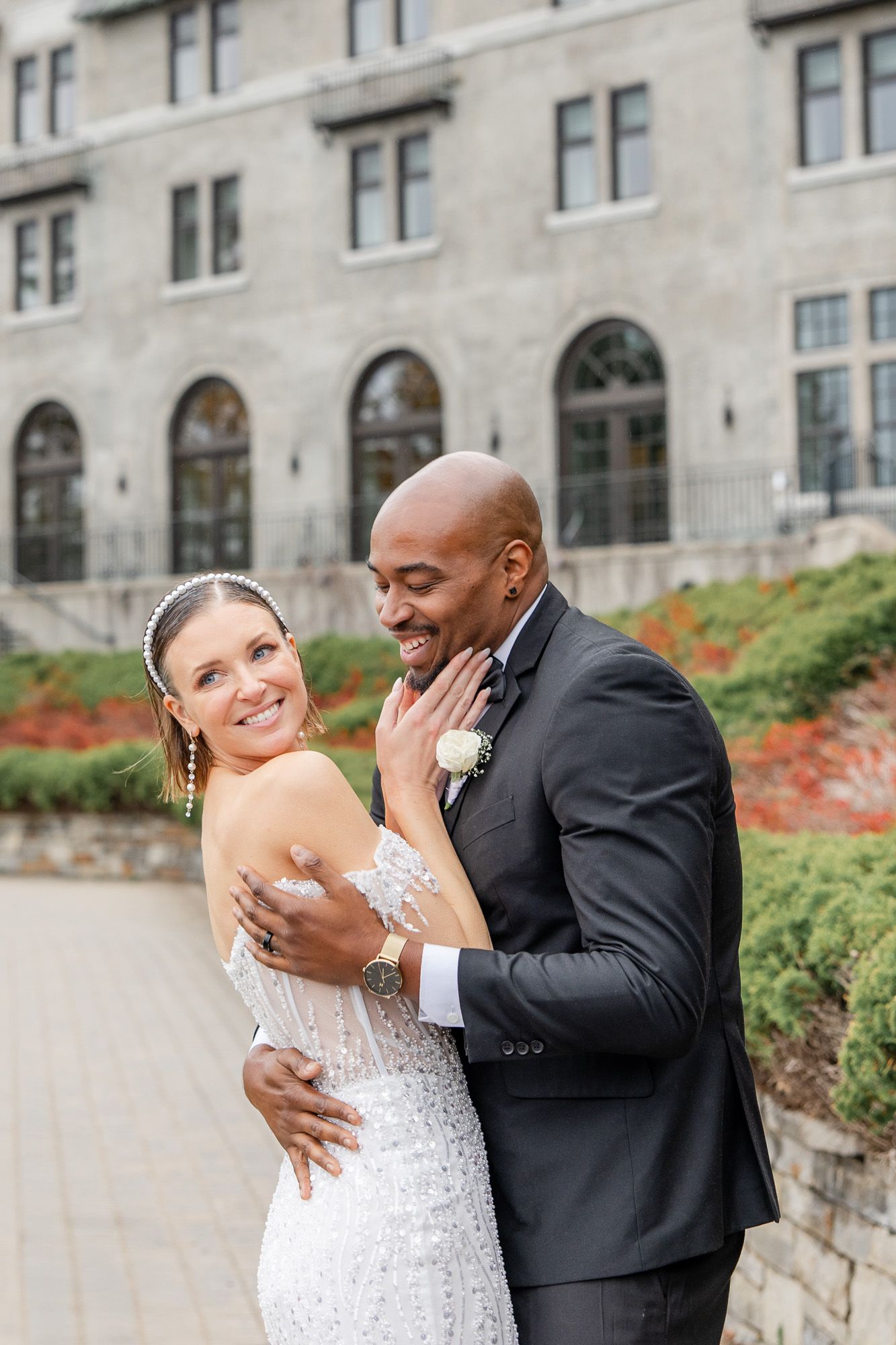 A happy couple shares romantic moments in formal wedding attire against a stone building backdrop.