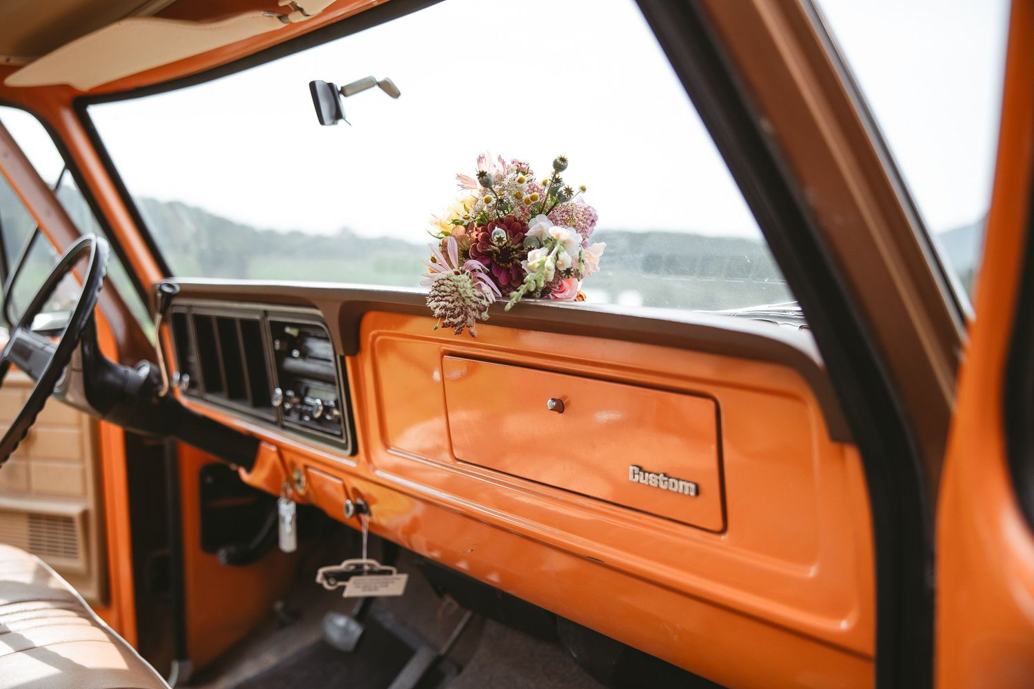 Tableau de bord d’un camion vintage orange avec bouquet floral rose et violet, photographie de mariage à Bromont