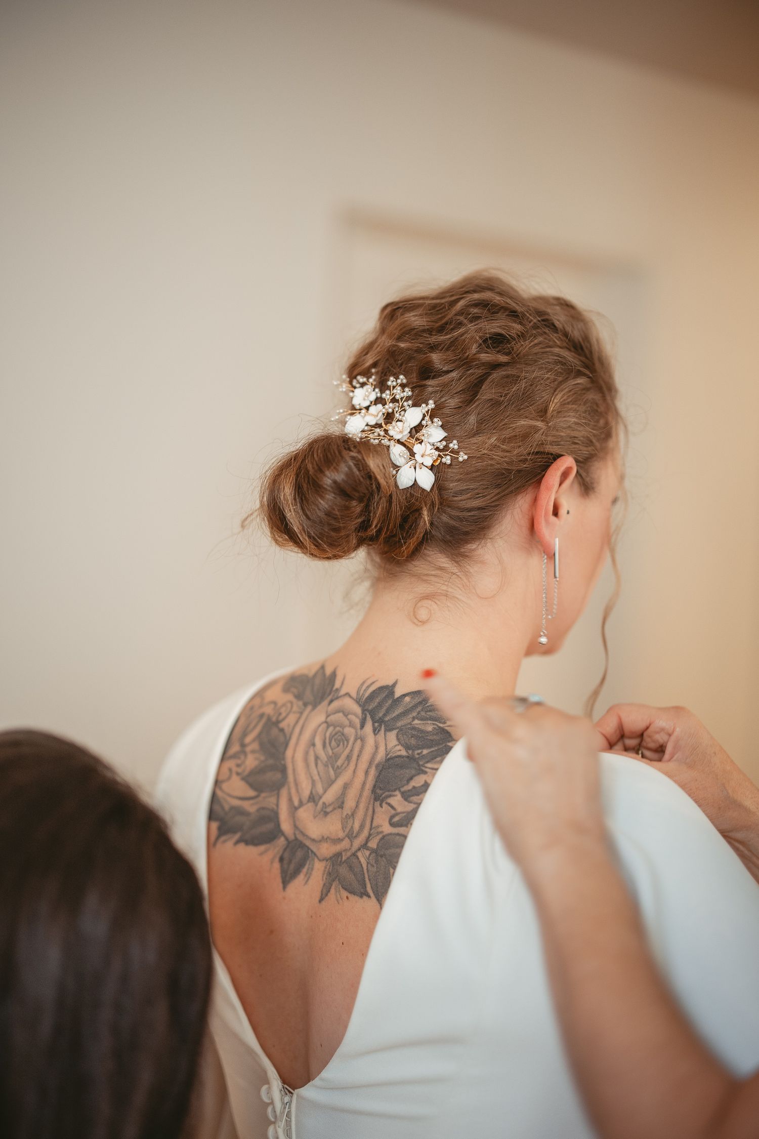 Gros plan d’une mariée vêtue de blanc, révélant un tatouage floral délicat et des accessoires de cheveux raffinés lors des préparatifs.