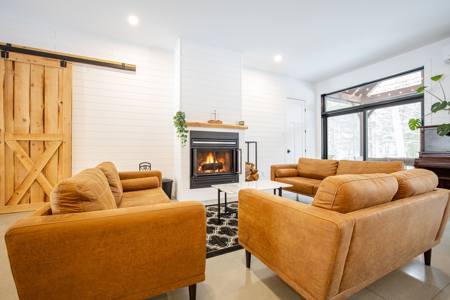 Salon de style ferme moderne avec canapés en cuir beige et porte de grange coulissante, baigné de lumière naturelle