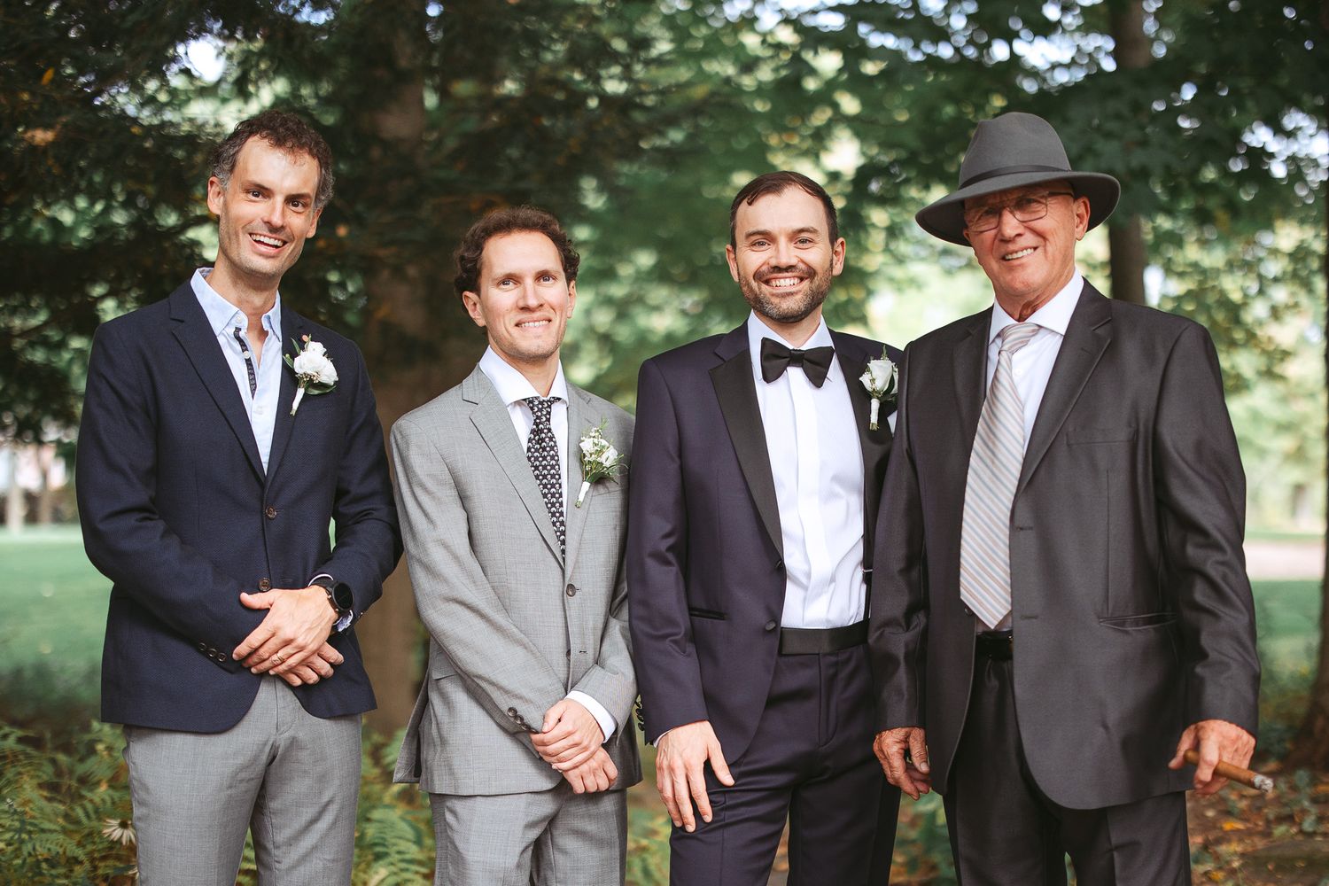 Groupe de garçons d’honneur en complets gris et chapeaux noirs posant ensemble pour des photos de mariage en extérieur