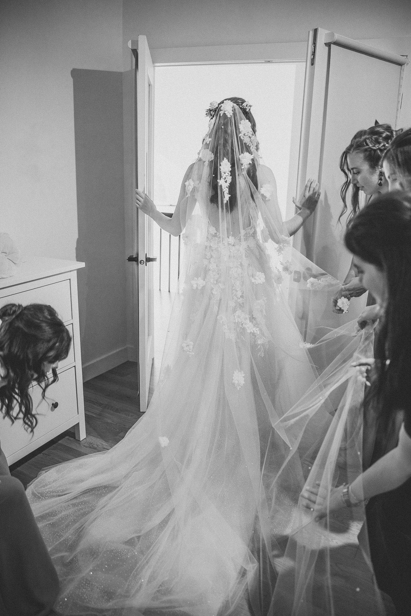 Photo de mariage en noir et blanc montrant un long voile fluide et une robe blanche disposés dans une pièce