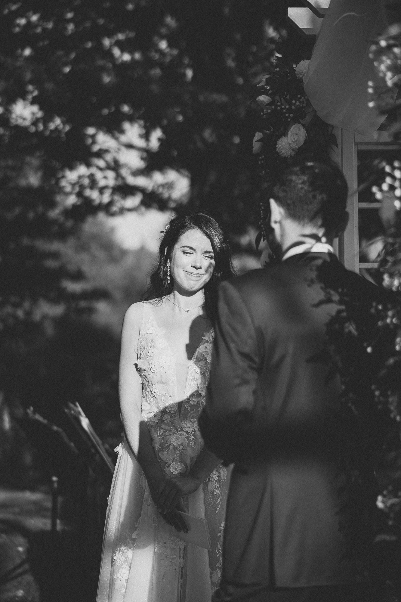 Photo de mariage en noir et blanc montrant un moment romantique entre la mariée en dentelle et le marié sous les arbres, en Estrie