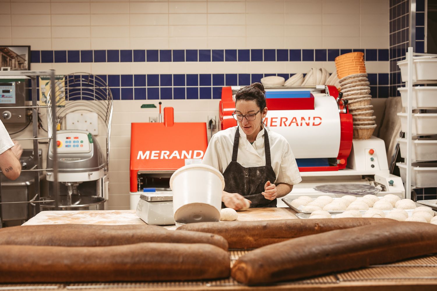 Professional bakery kitchen with long wooden work tables and equipment.