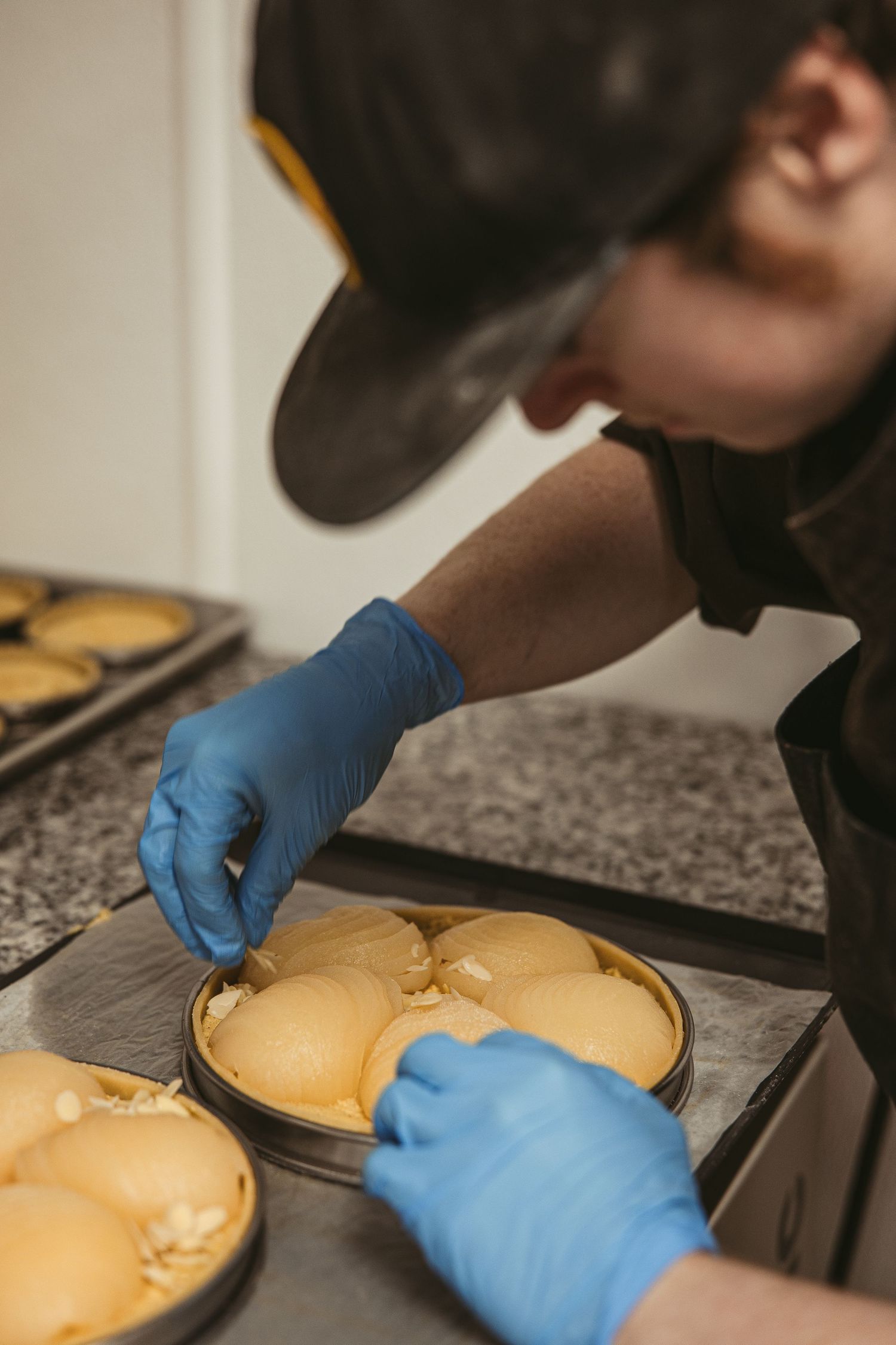 Close-up of hands with blue gloves working on baked goods in kitchen.