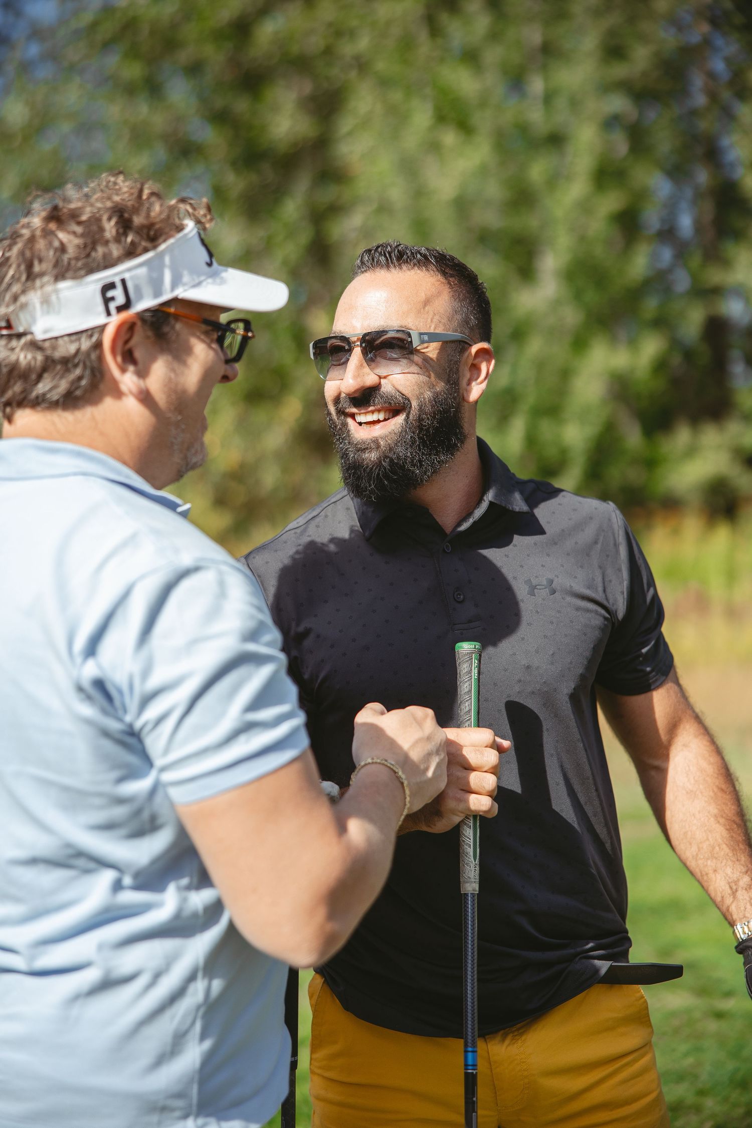 Two golfers share a friendly moment on the golf course while holding golf clubs on a sunny day.