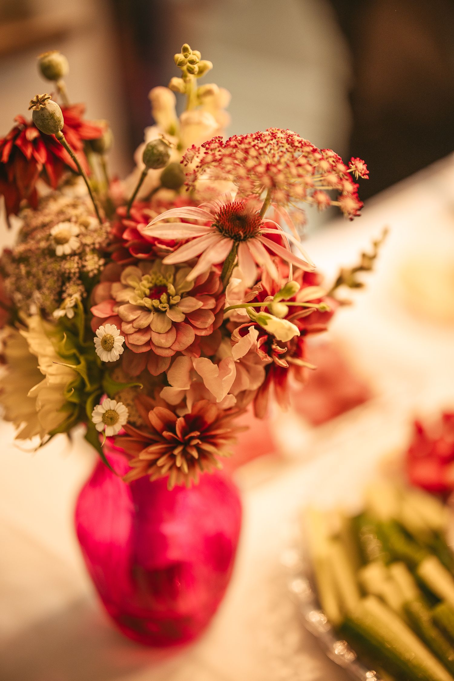 Fleurs de zinnias roses et corail disposées dans des vases en verre magenta, créant un centre de table élégant