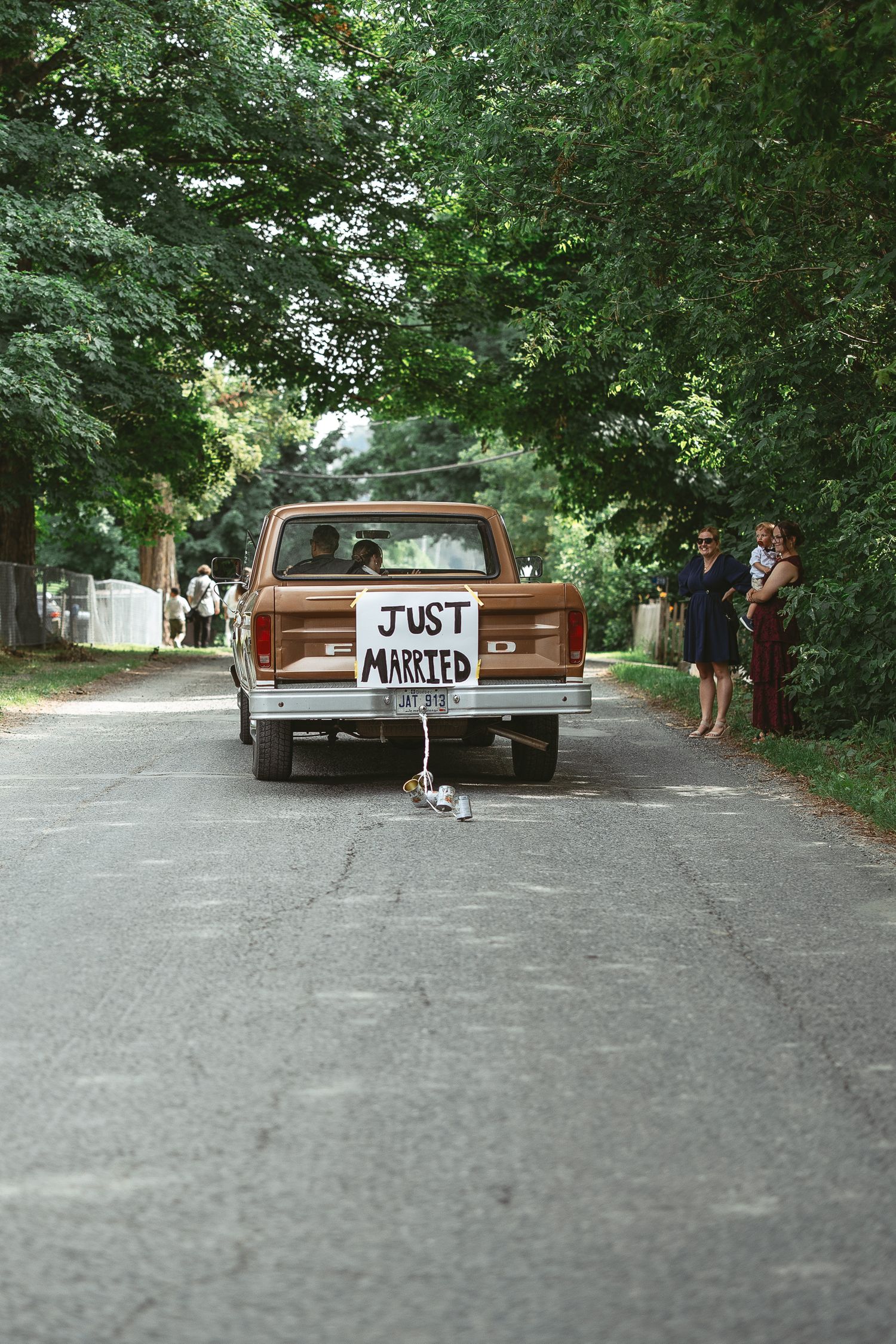 Pickup vintage brun avec inscription “Just Married”, stationné sur une route bordée d’arbres lors d’un mariage