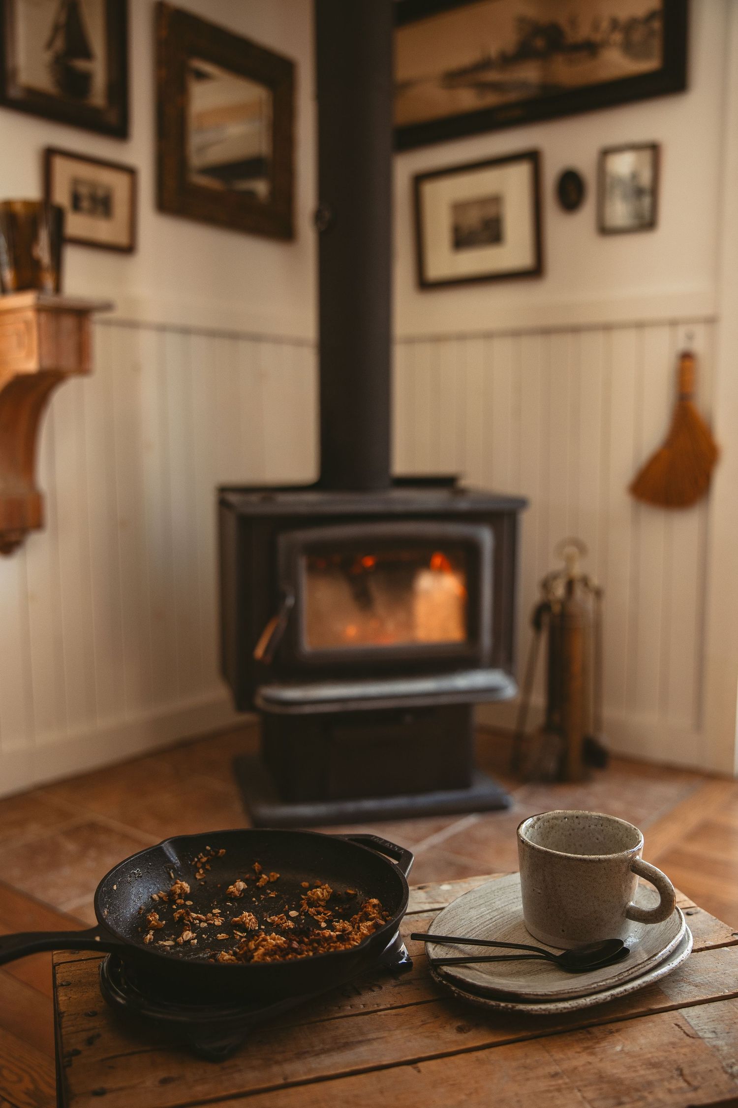 A rustic wooden table setting with vintage frames on white walls, cast iron cookware, and a wood burning stove.