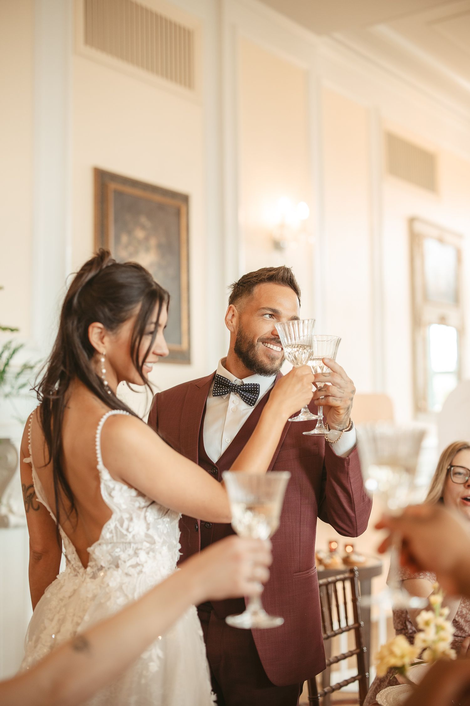 A couple in wedding attire raises their glasses in a celebratory toast during their reception.