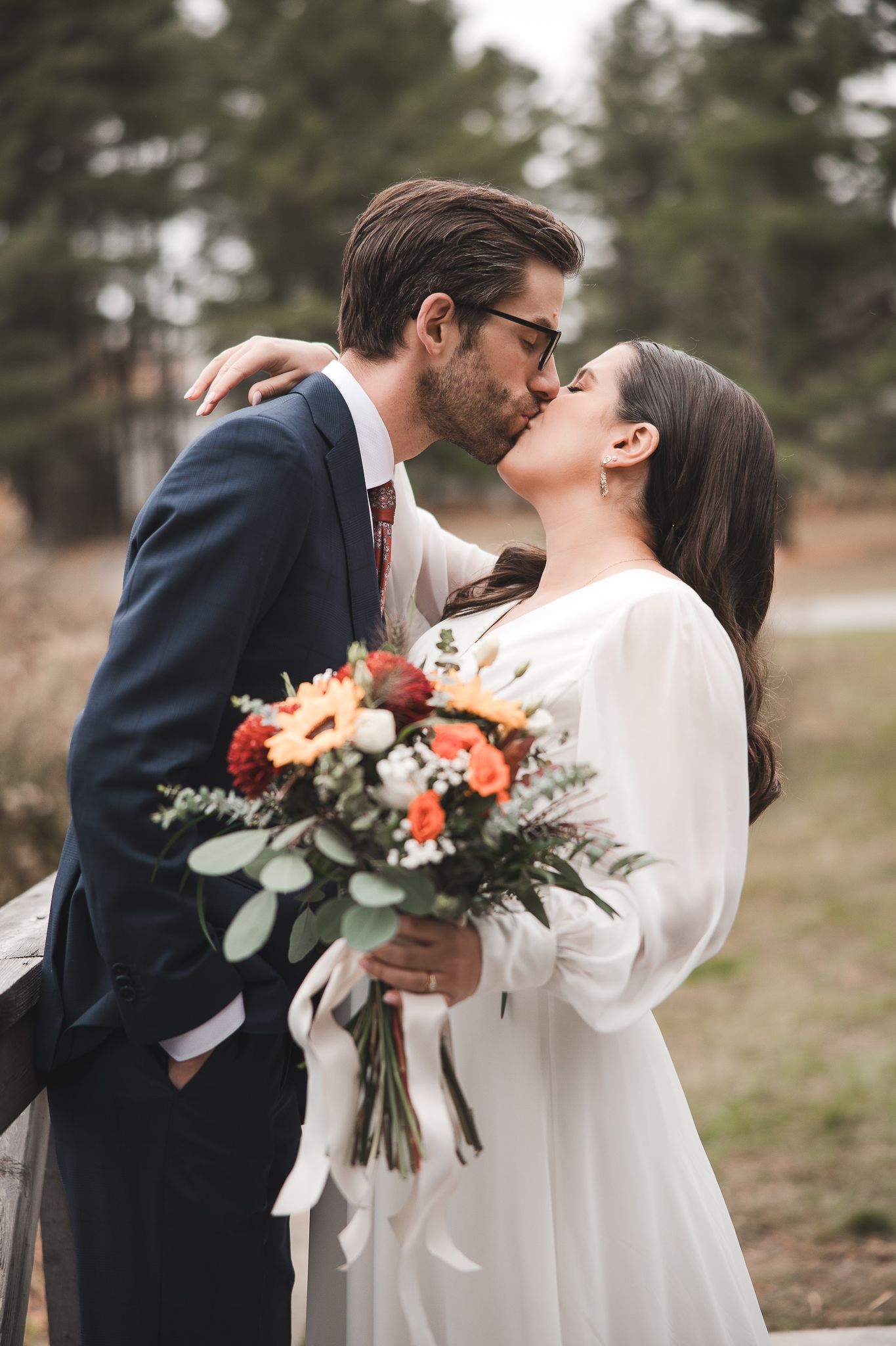 Les nouveaux mariés partagent des moments intimes en plein air, tenant des bouquets floraux aux teintes automnales, devant un décor de conif