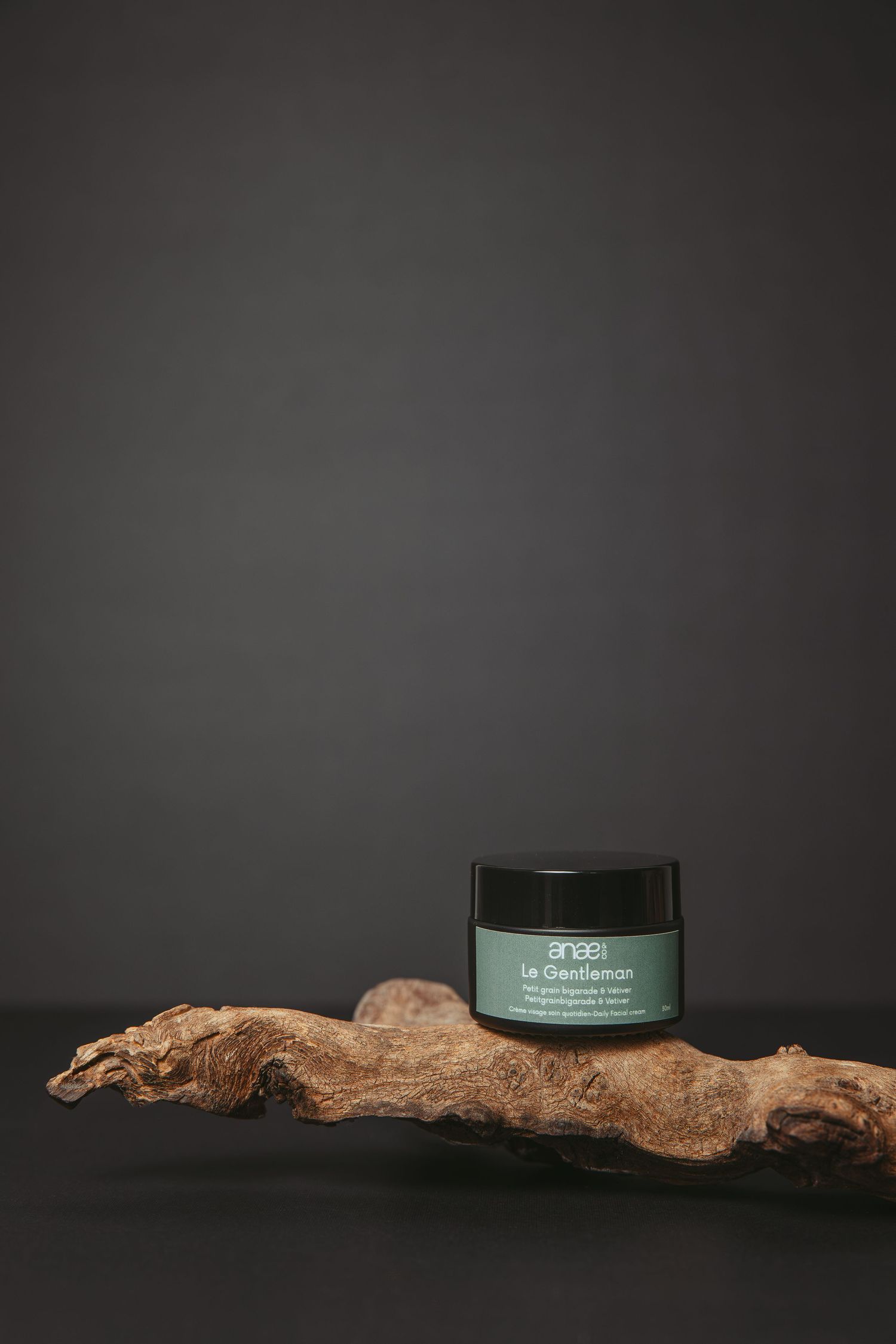 Dark skincare product jar displayed on natural driftwood against black background.