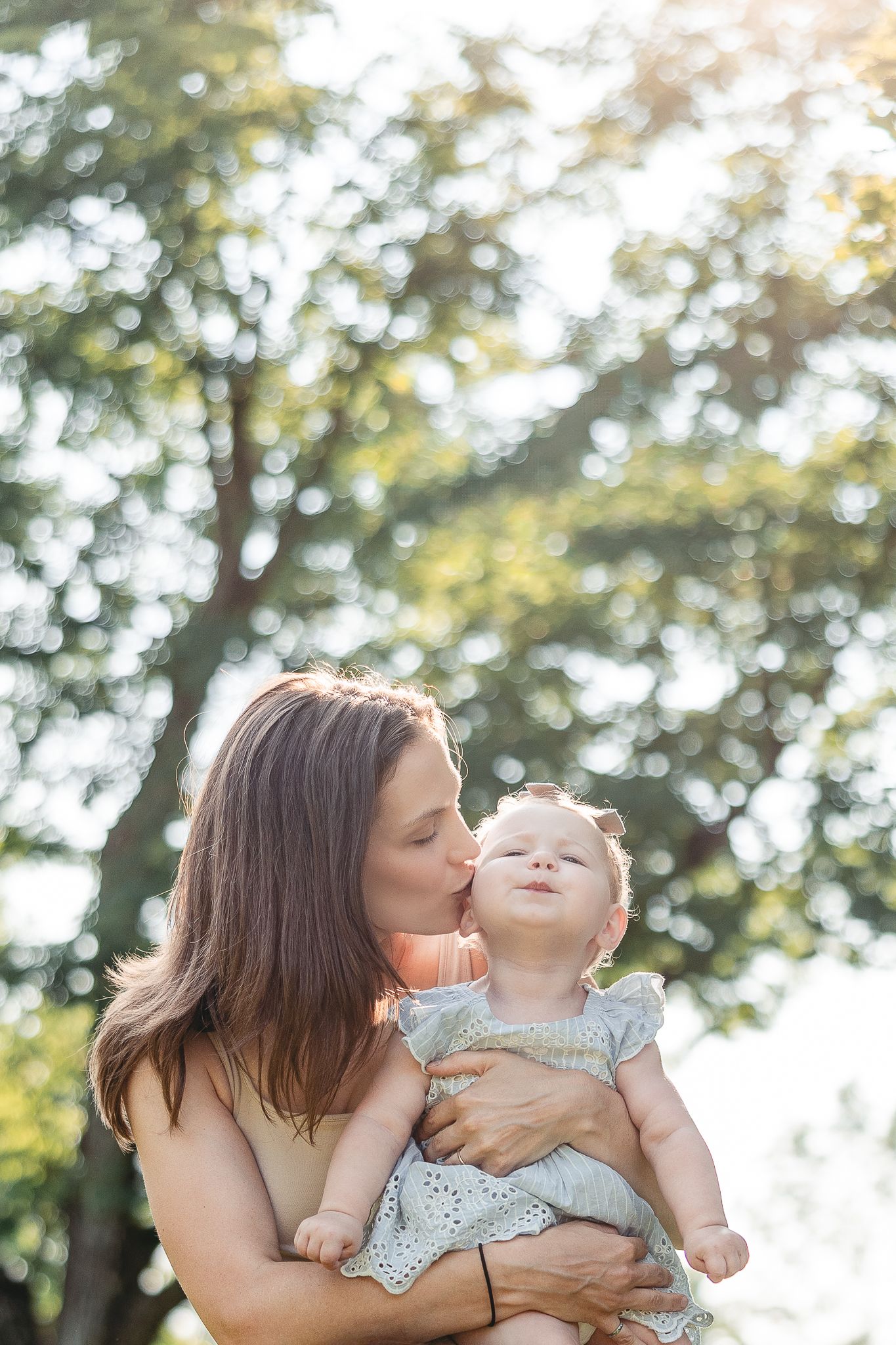 Moment tendre en famille capturé en extérieur sous une lumière chaude, avec des arbres en arrière-plan pour une ambiance naturelle et douce