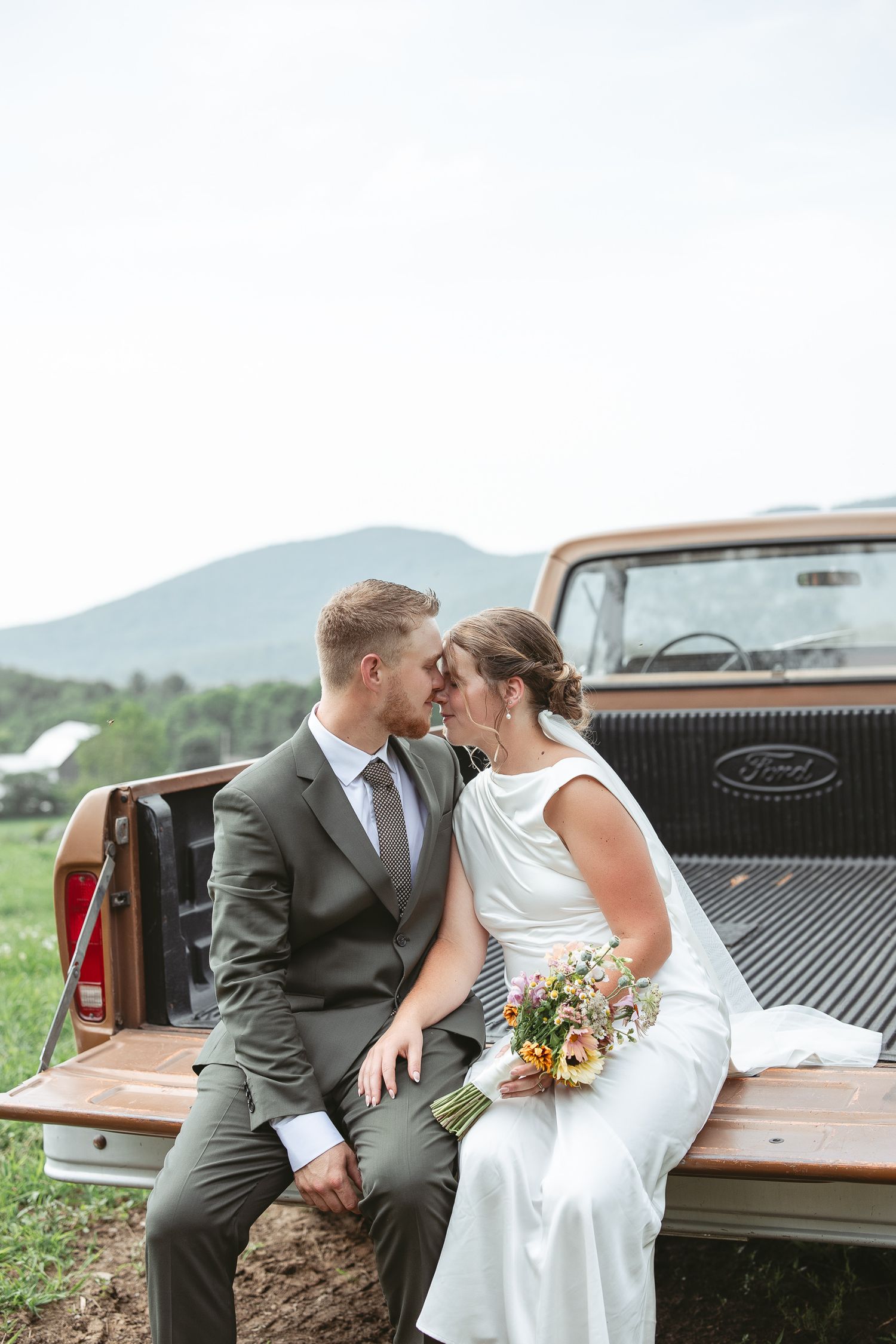 Couple de mariés partageant un moment romantique assis à l’arrière d’un pickup Ford vintage, dans un décor champêtre