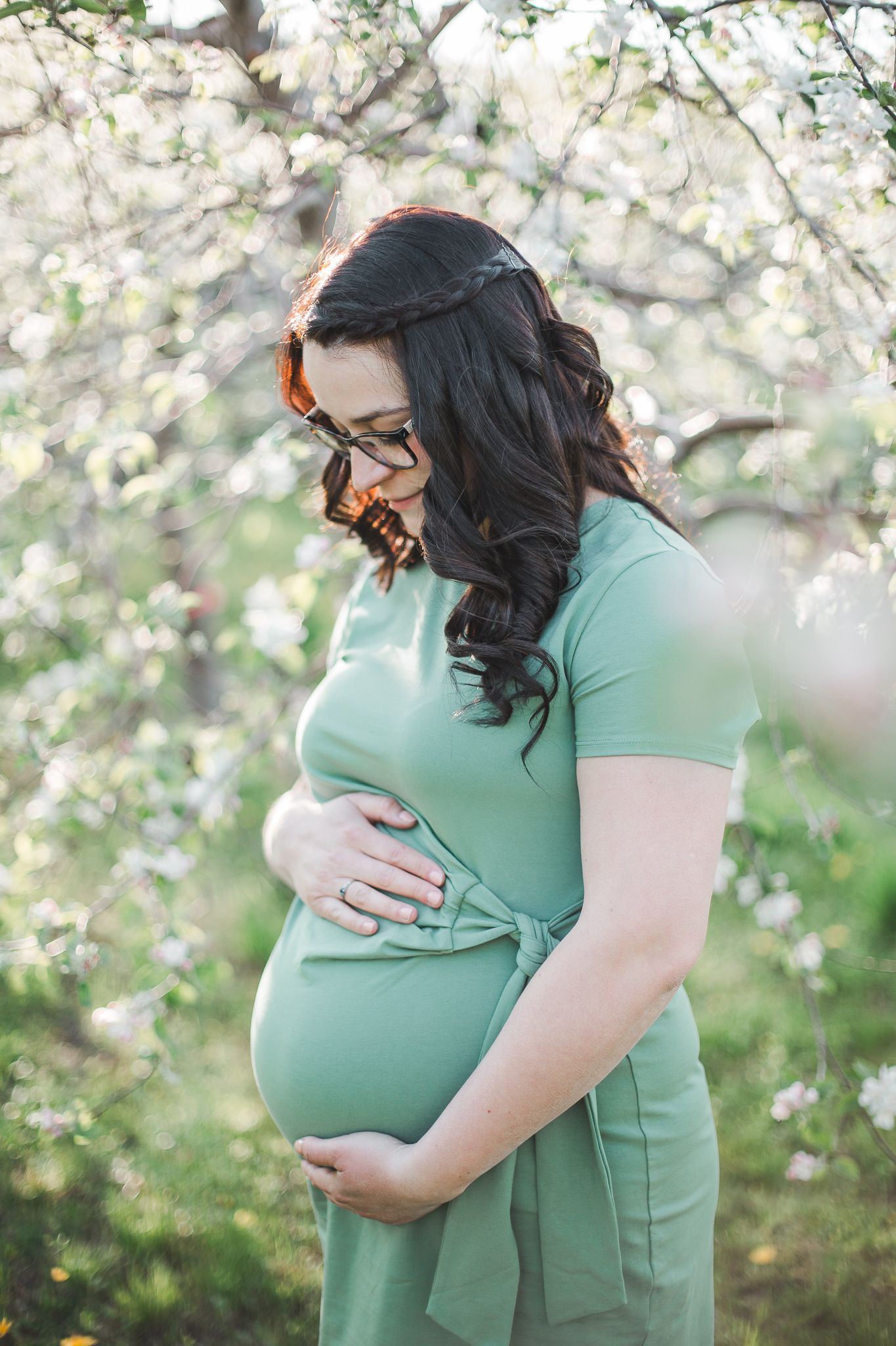 femme enceinte en robe vert menthe parmi arbres en fleurs au printemps, capturée pour moments doux et élégants