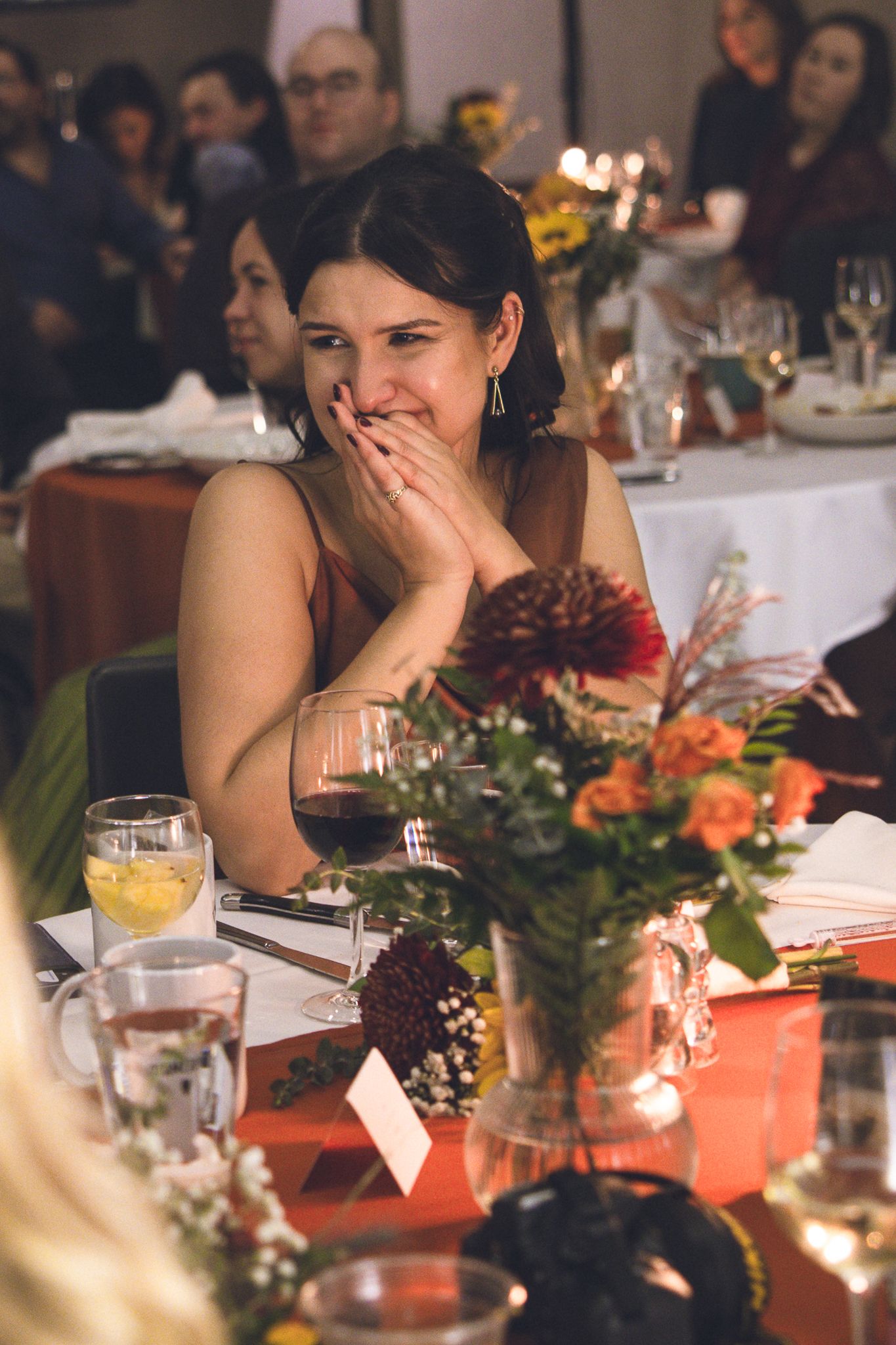 Des invités de réception de mariage sont assis à une table élégamment décorée, avec des centres de table floraux et des accents orange