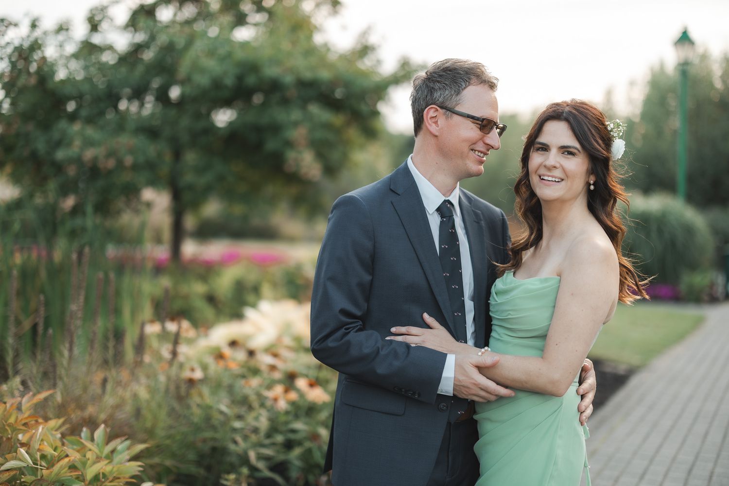 Couple en tenue élégante partageant un moment romantique sur une passerelle en bois entourée de verdure luxuriante