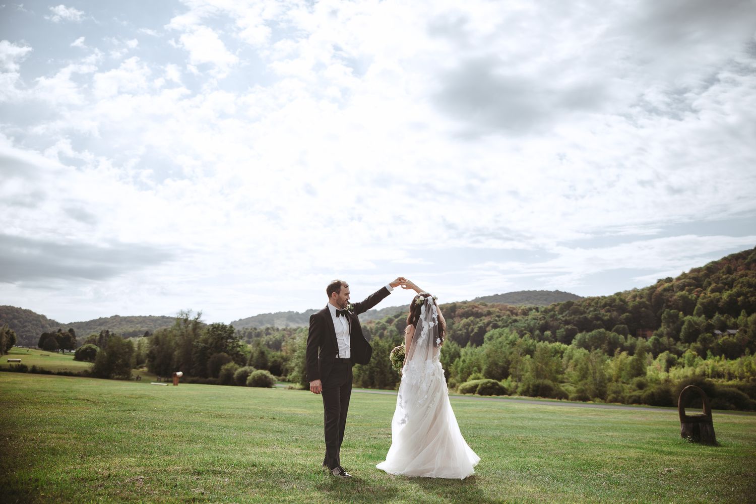 Couple en tenue de mariage debout dans une prairie de montagne, ciel nuageux spectaculaire en arrière-plan, en Estrie