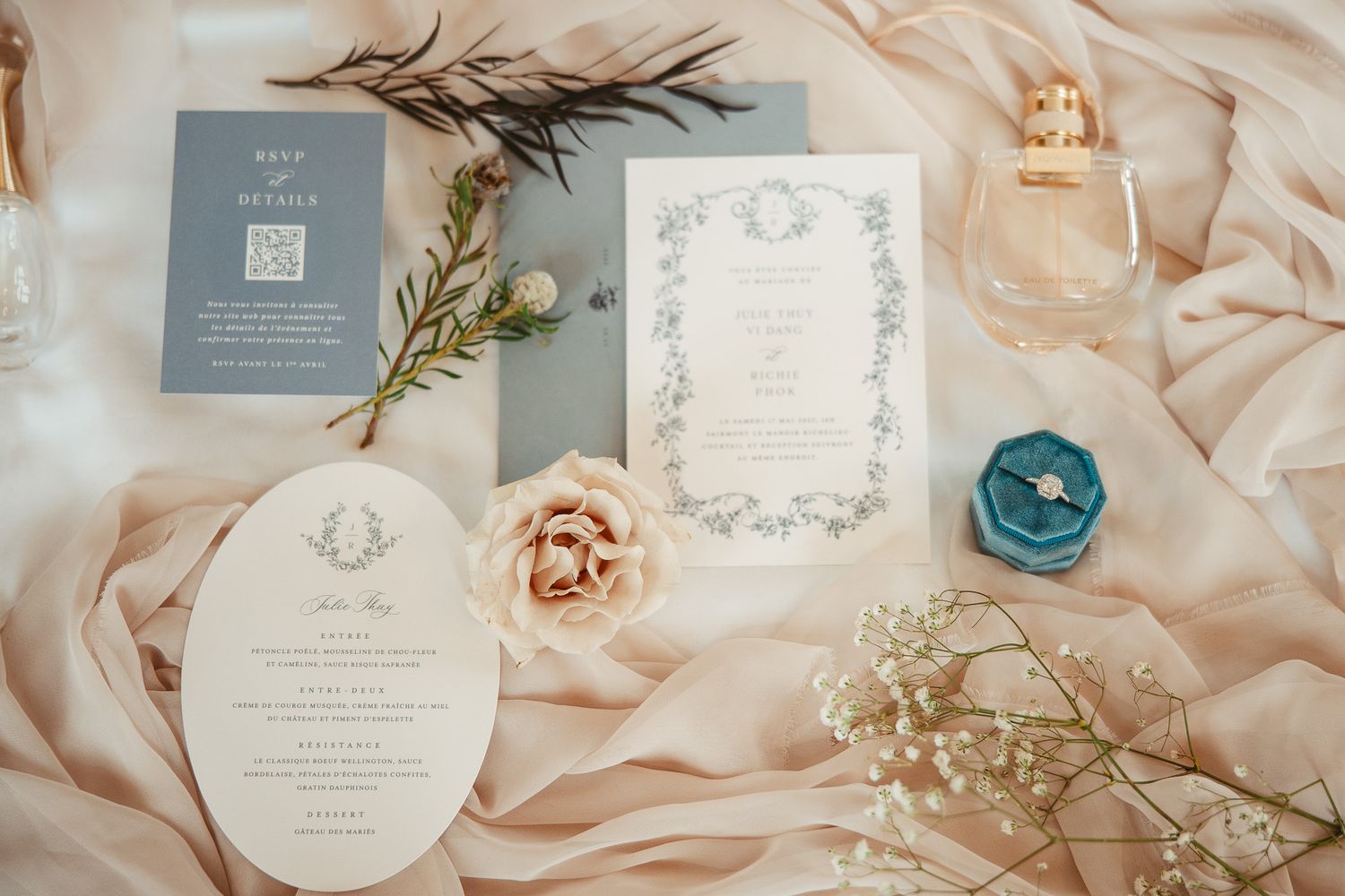 Suite de faire-part de mariage avec détails floraux, disposée sur un tissu blush avec parfum et fleurs délicates