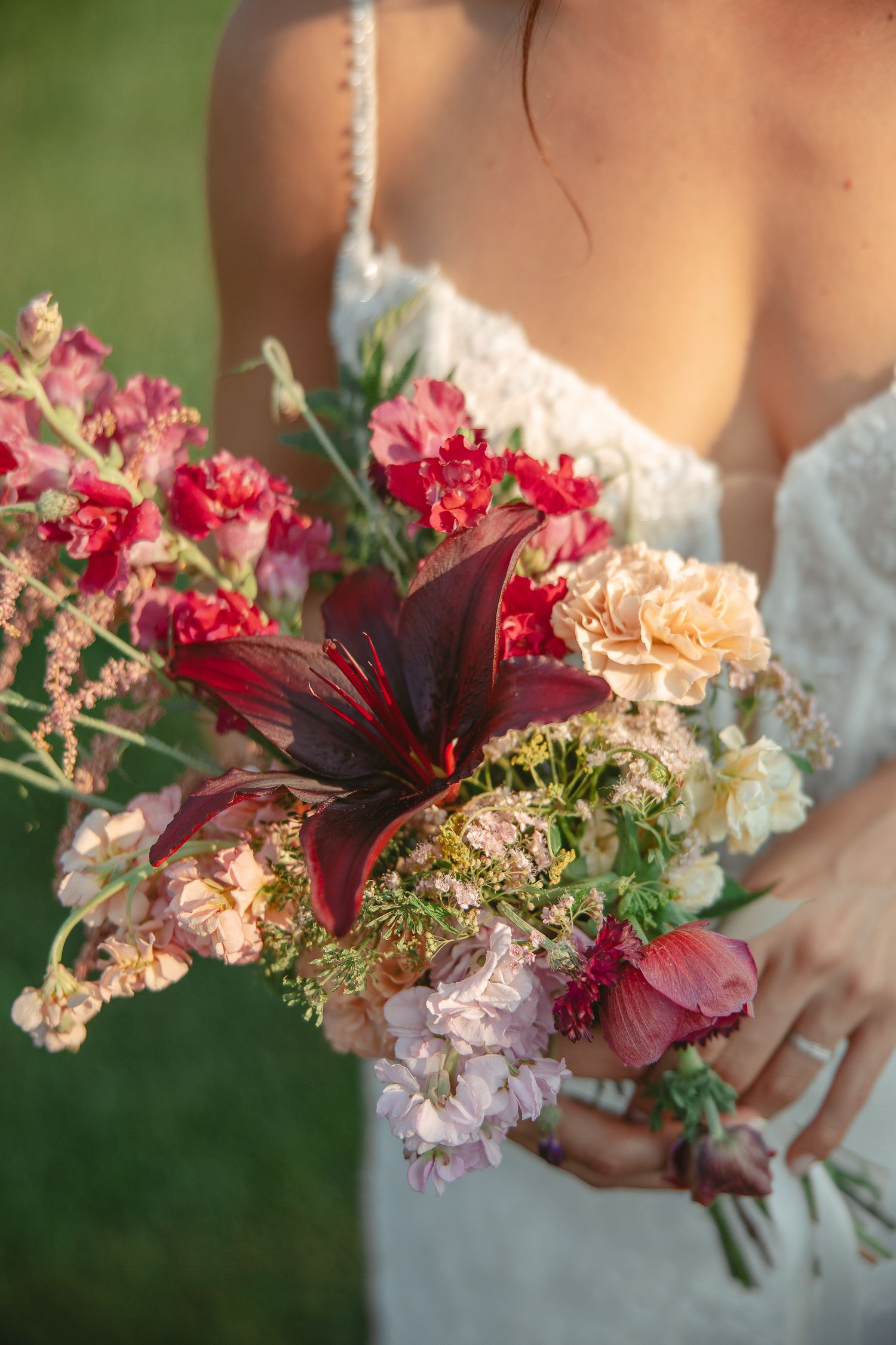 Bouquet de mariée coloré composé d’œillets roses, de dahlias bourgogne et de fleurs pêche, photographié sur fond vert.