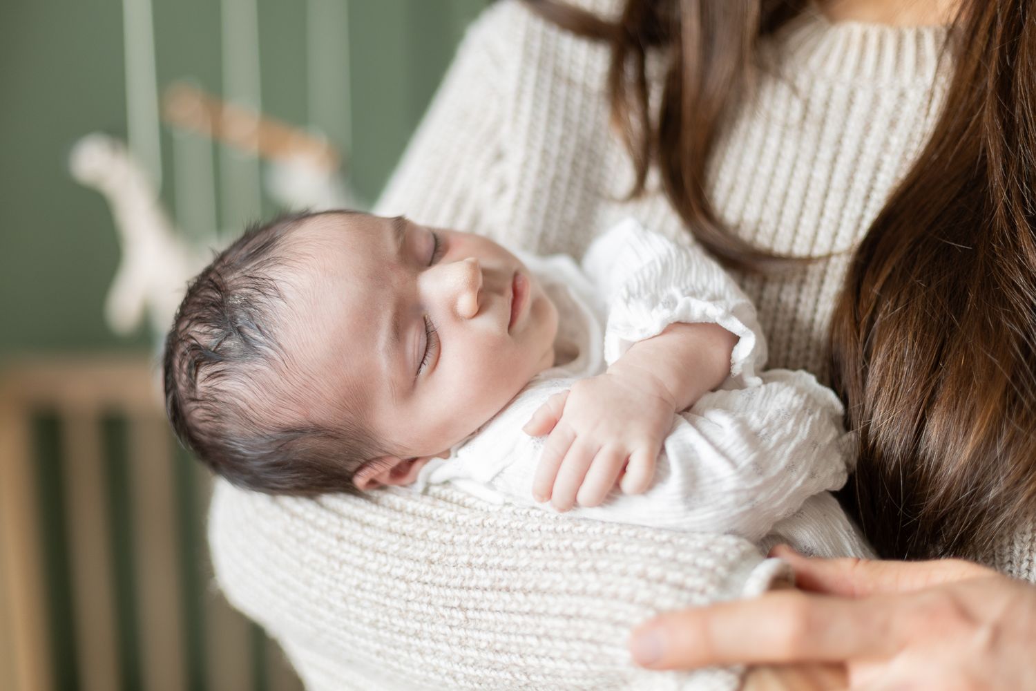 Bébé paisible dans les bras d’un parent à Bromont/Estrie, fond vert doux, capturé pour intimité, tendresse et souvenirs chaleureux.