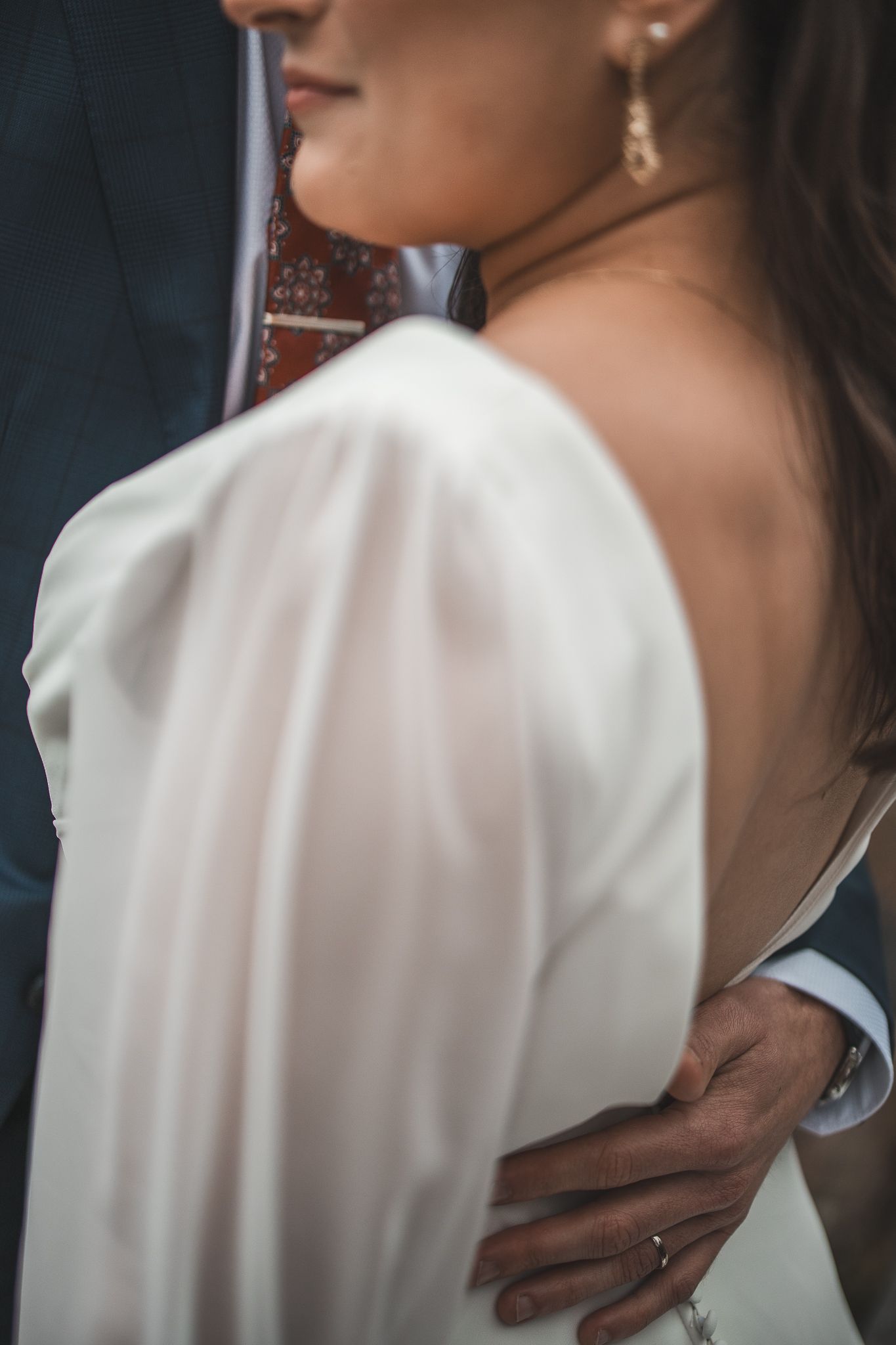 Détails en gros plan de la manche et de l’encolure d’une robe de mariée blanche, sur un fond sombre.