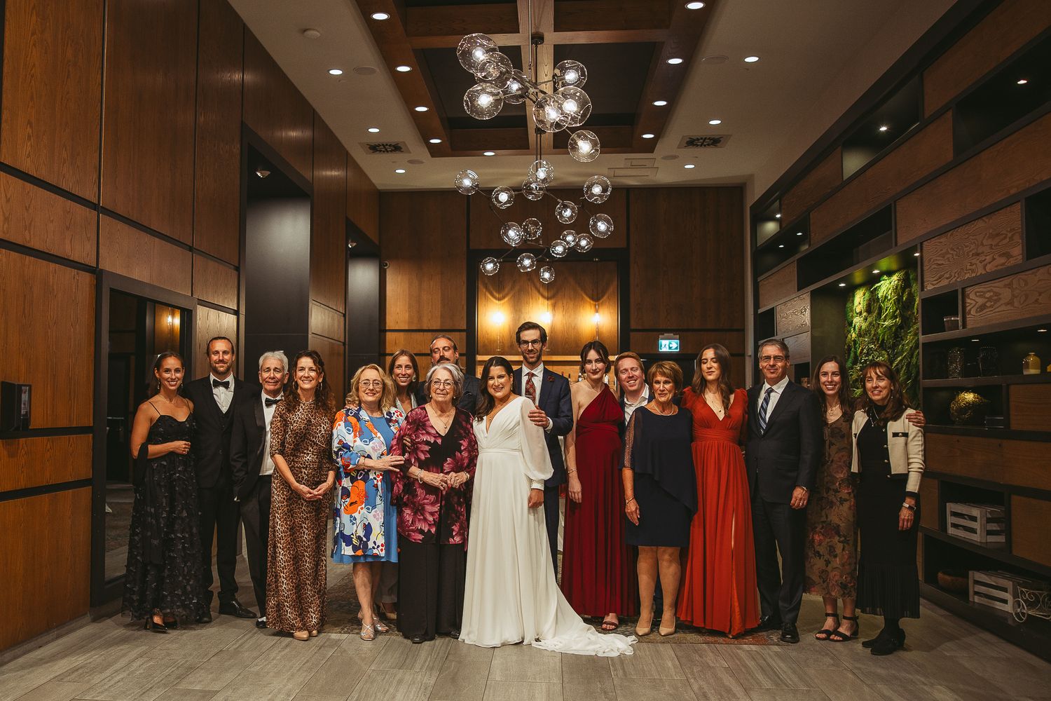 Des membres du cortège de mariage, vêtus de tenues élégantes, se rassemblent dans un corridor faiblement éclairé aux murs de brique.