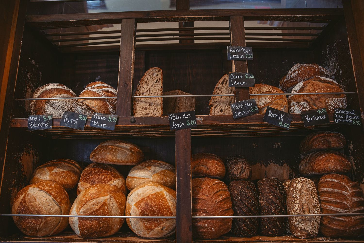 Fresh artisan bread loaves displayed on wooden shelves in a rustic bakery setting.