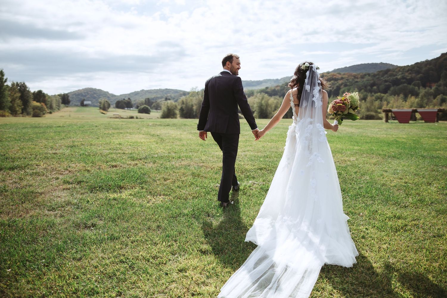 A couple in wedding attire walks through scenic mountain meadows on their special day.