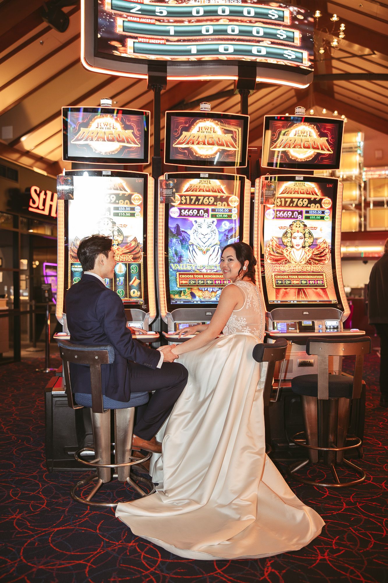 Couple en tenue de mariage jouant aux machines à sous, la robe blanche de la mariée fluide au Casino de Charlevoix