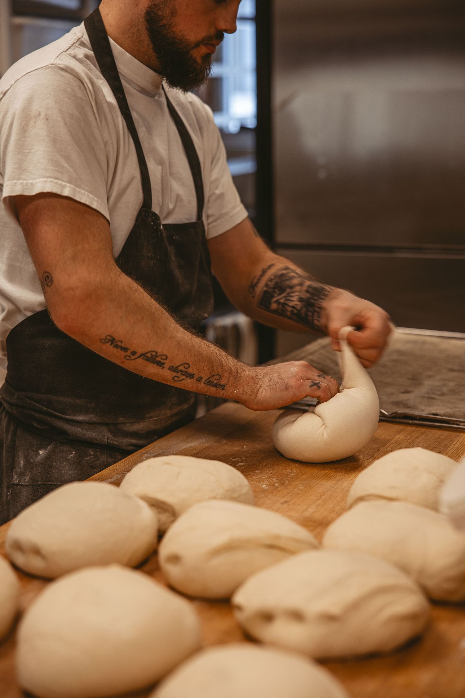 Baker kneading and shaping bread dough on wooden work surface.