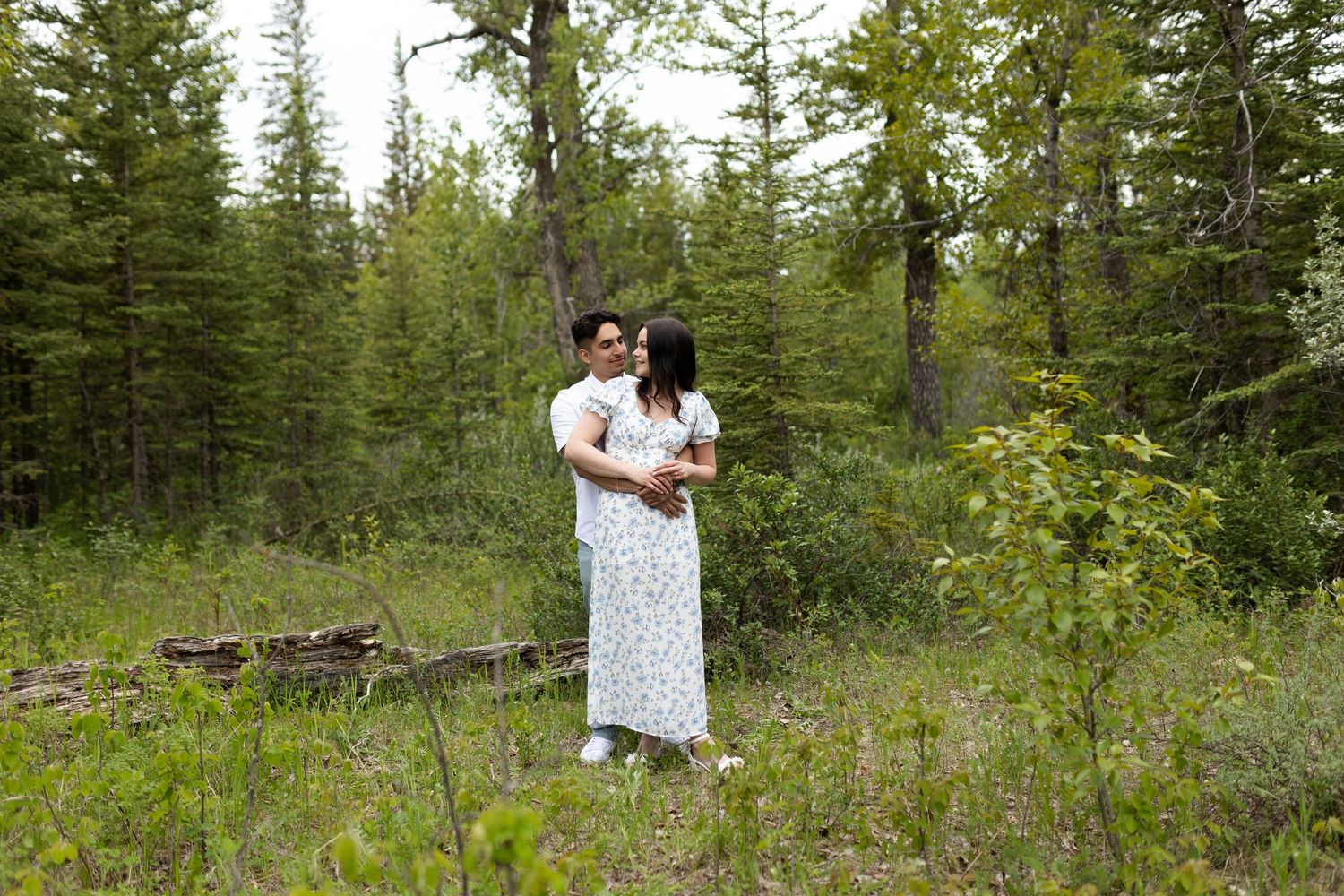 A couple shares a romantic moment while standing in a lush forest clearing.