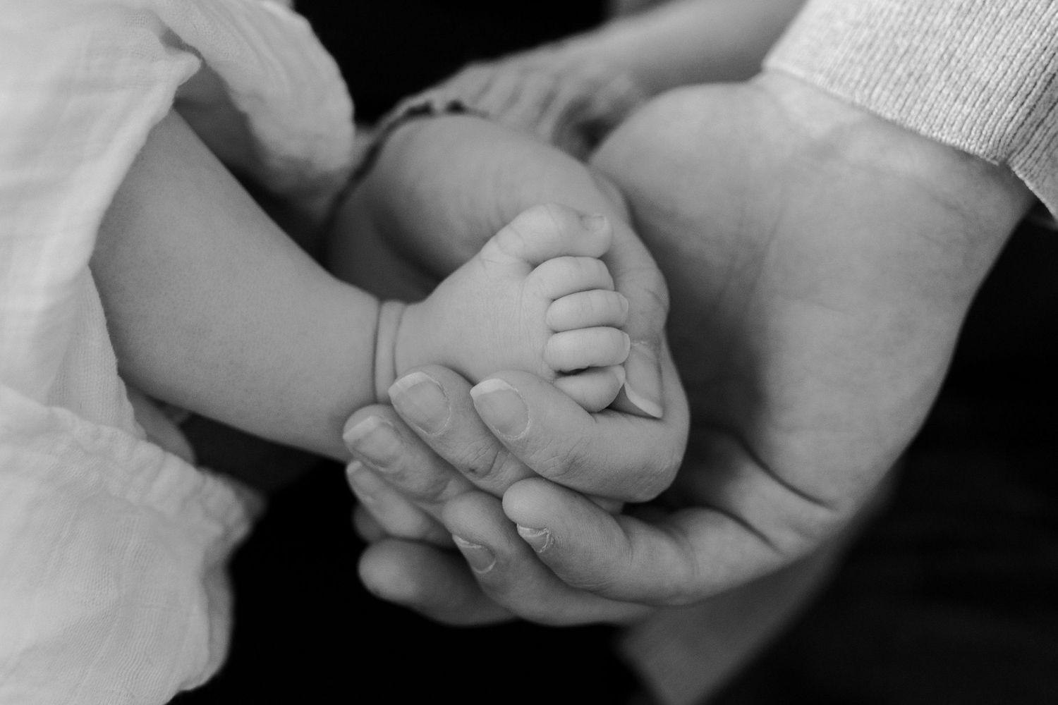 Close-up black and white photo of baby's tiny feet being held in parent's hands.