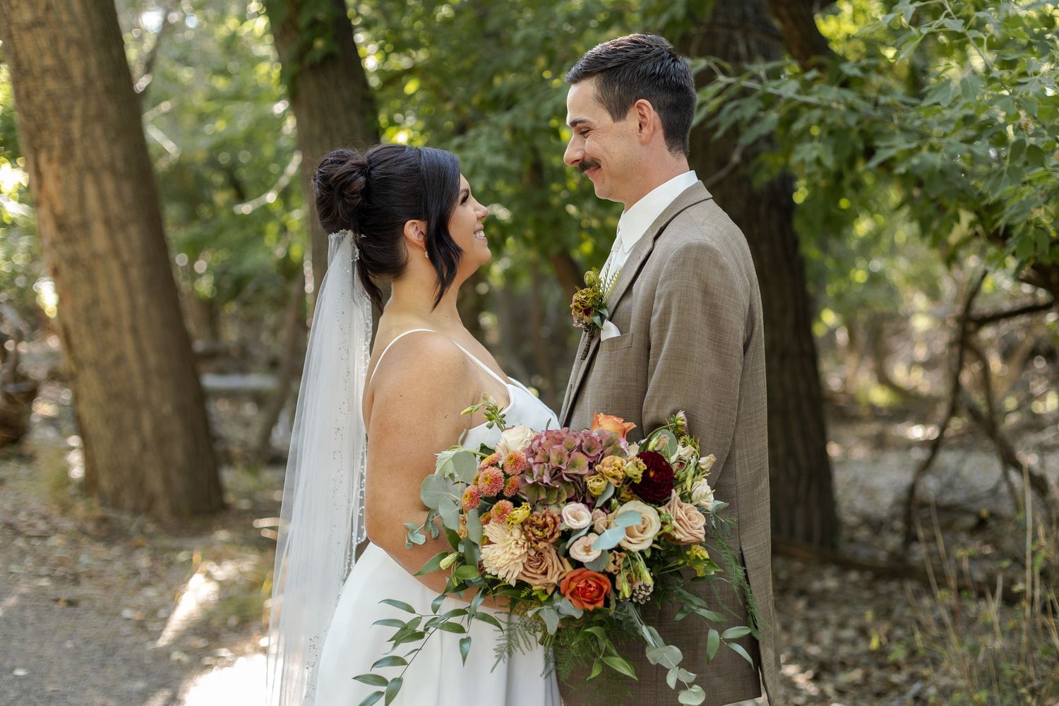 Newlywed couple shares intimate moments in a sunlit wooded area during their outdoor wedding photo session.