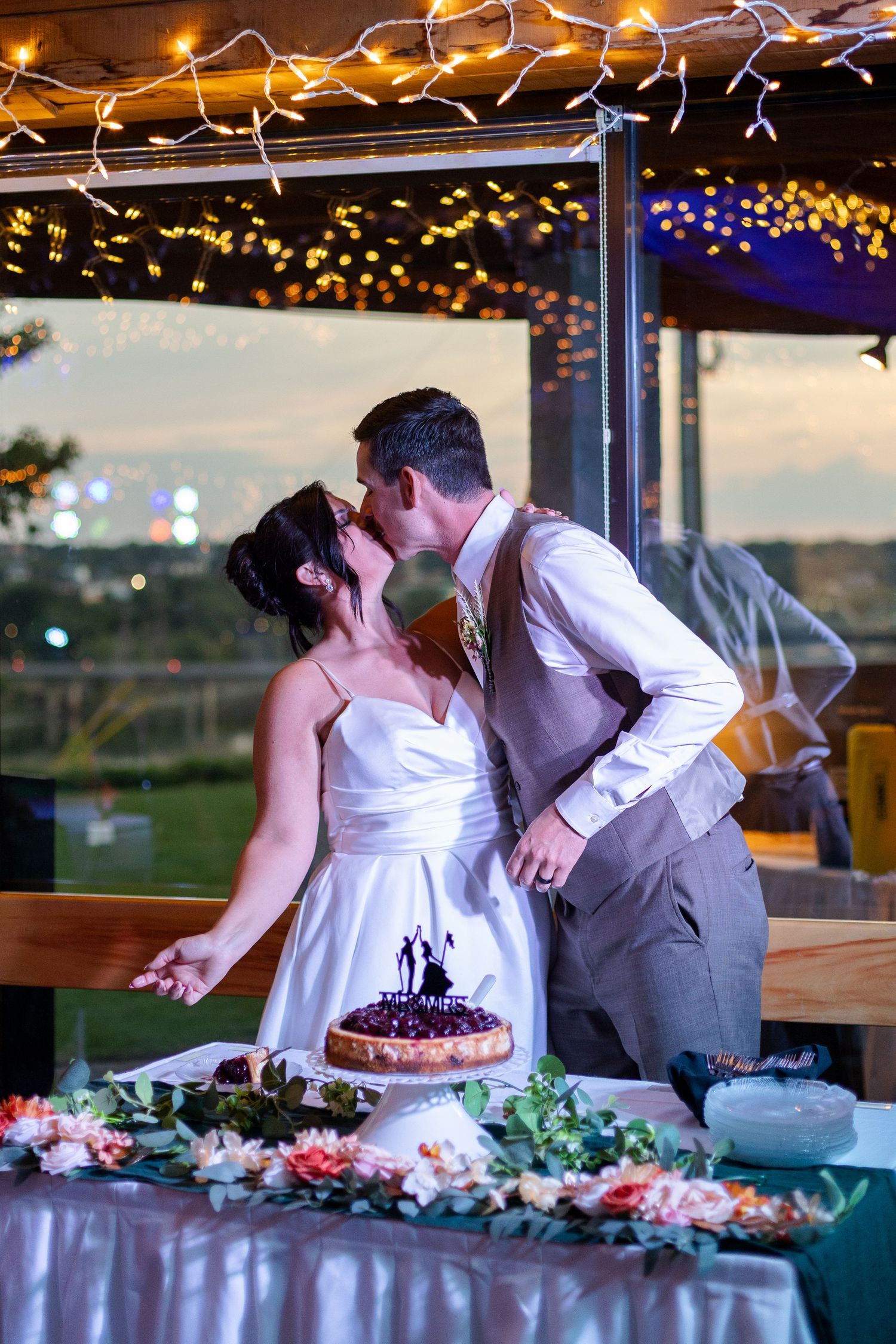Couple cuts their wedding cake under twinkling lights at evening reception.