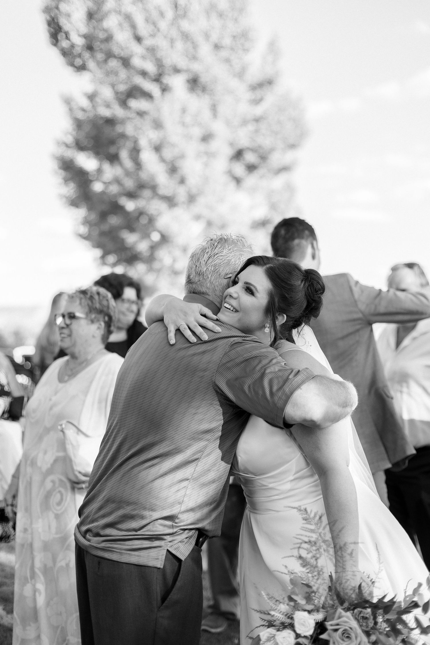 A black and white photo shows a group of people embracing in an emotional moment at an outdoor celebration.