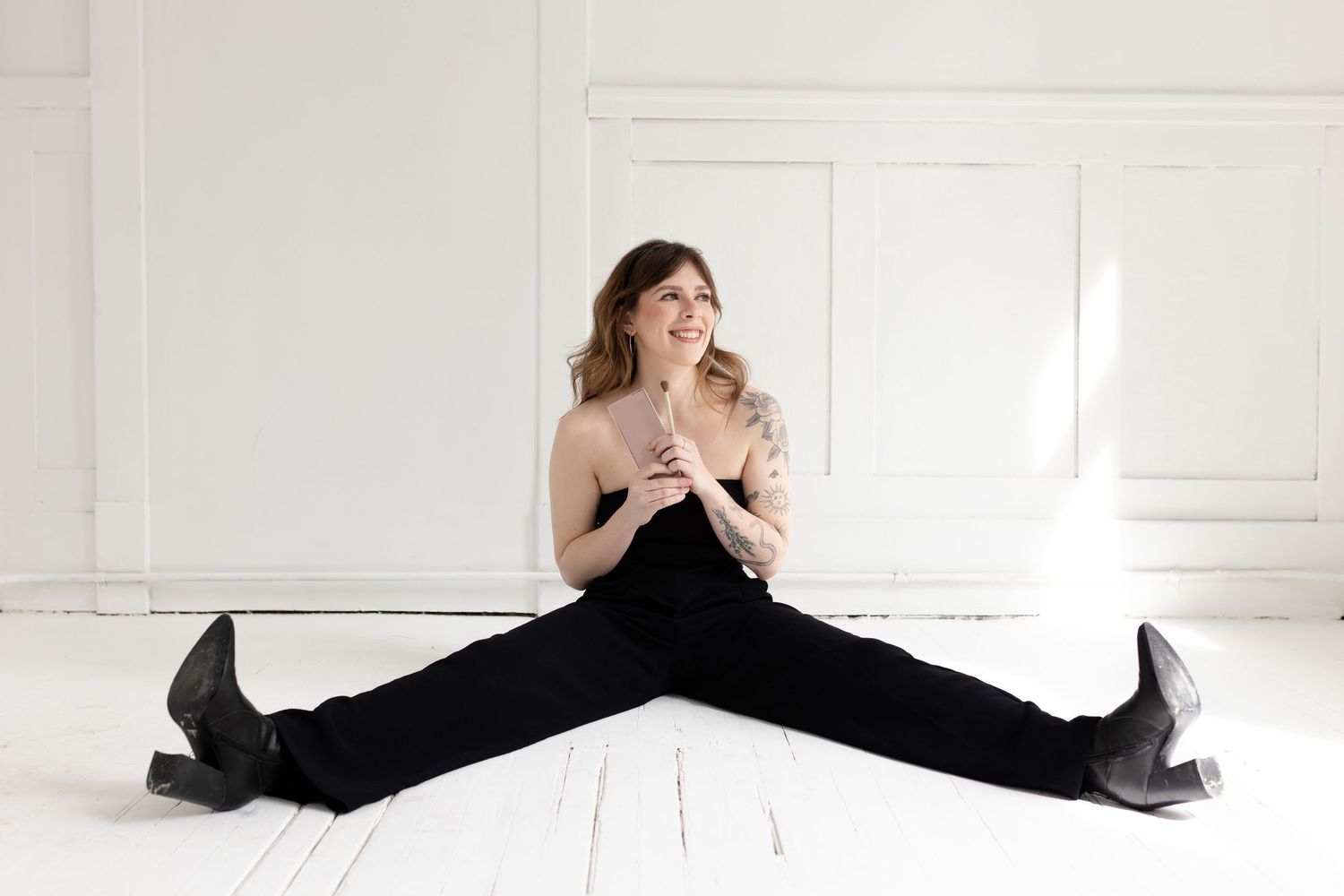 Professional model poses dramatically in black outfit against white studio backdrop.