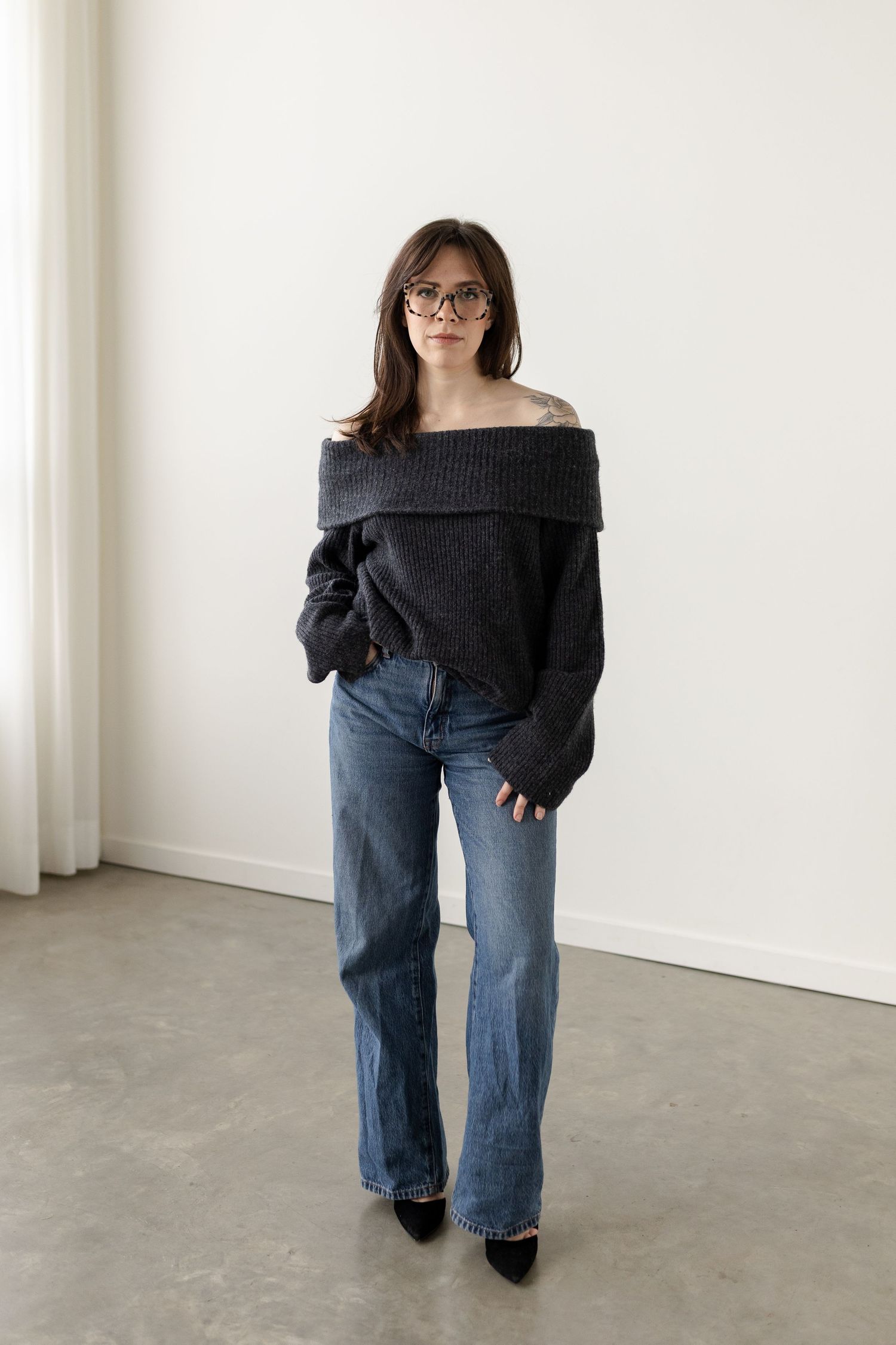A fashion photo series showing a person in a black off-shoulder sweater and relaxed blue jeans in different poses.