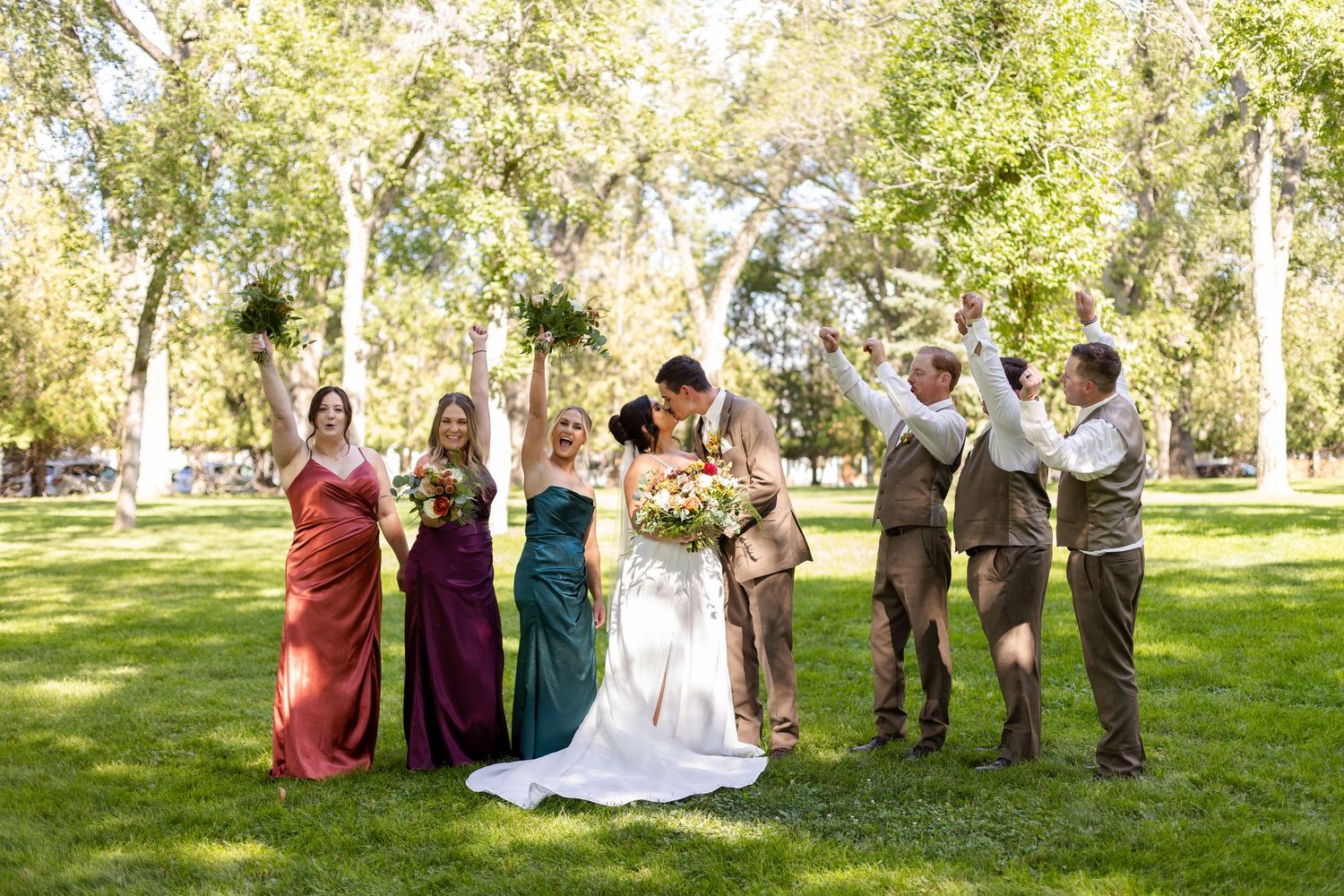 Wedding party poses playfully on lush green lawn during outdoor summer celebration.